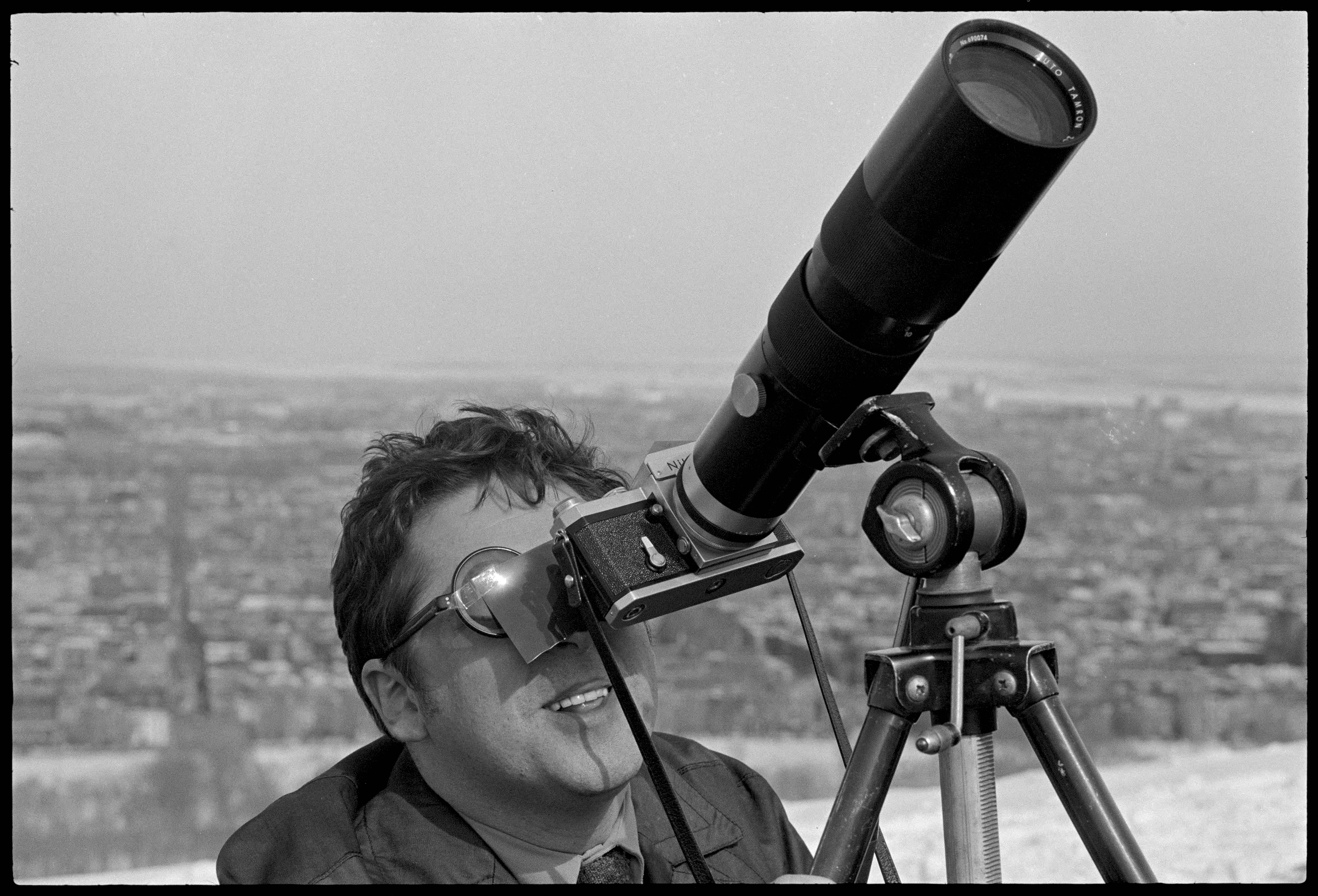 Homme portant lunettes fumées regardant dans l'objectif d'un appareil photo au long objectif.