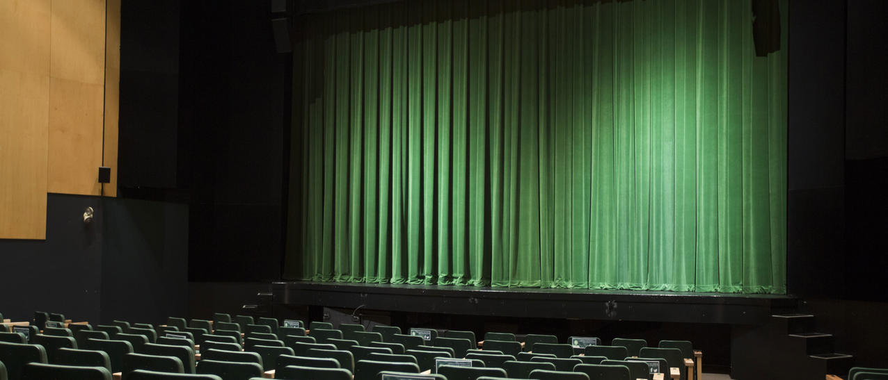 Salle de spectacle avec sièges et scène dotée d'un rideau vert.