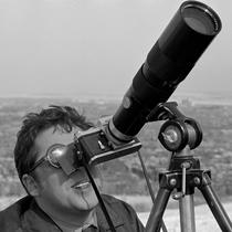 Homme portant lunettes fumées regardant dans l'objectif d'un appareil photo au long objectif.