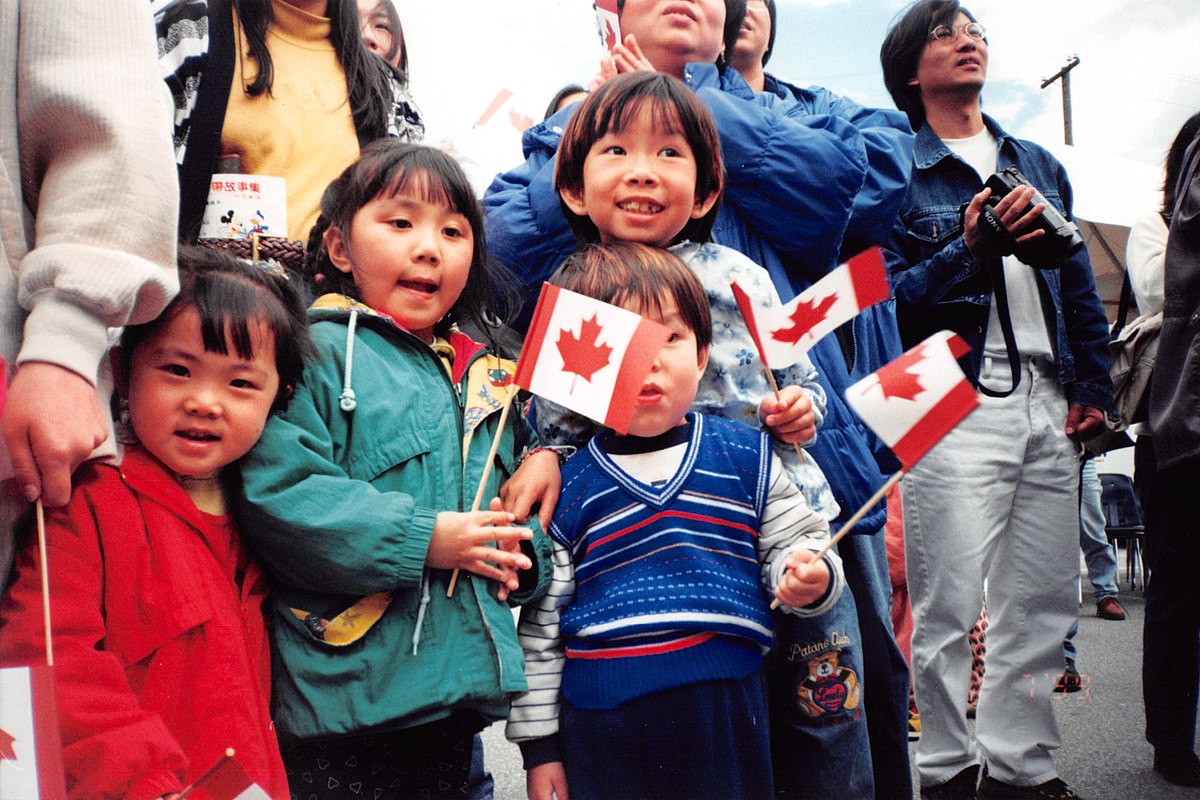 Enfants et adultes d’origine asiatique agitant de petits drapeaux du Canada.