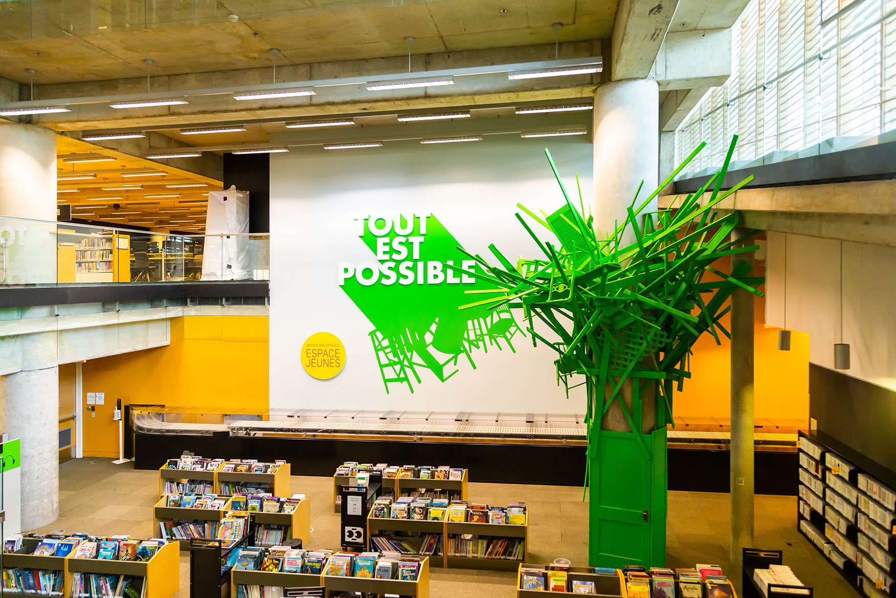 Rayons de livres jouxtant une installation d'art faite de matériaux recyclés, intitulée « Tout est possible ».