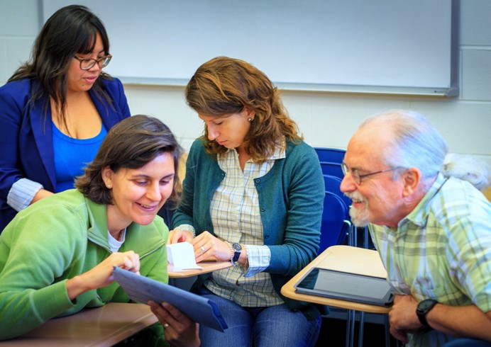 Groupe de quatre adultes, deux à l'avant plan regarde une tablette intelligente
