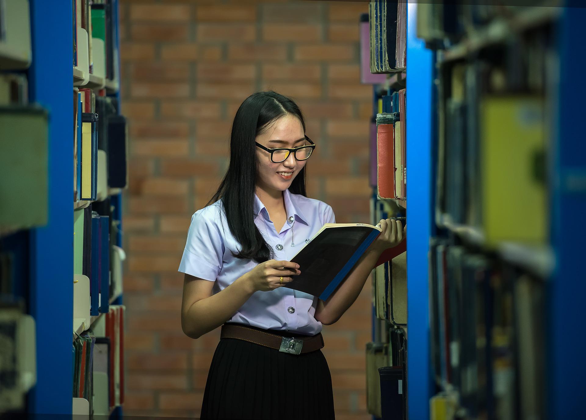 Jeune femme lisant un livre debout à la bibliothèque