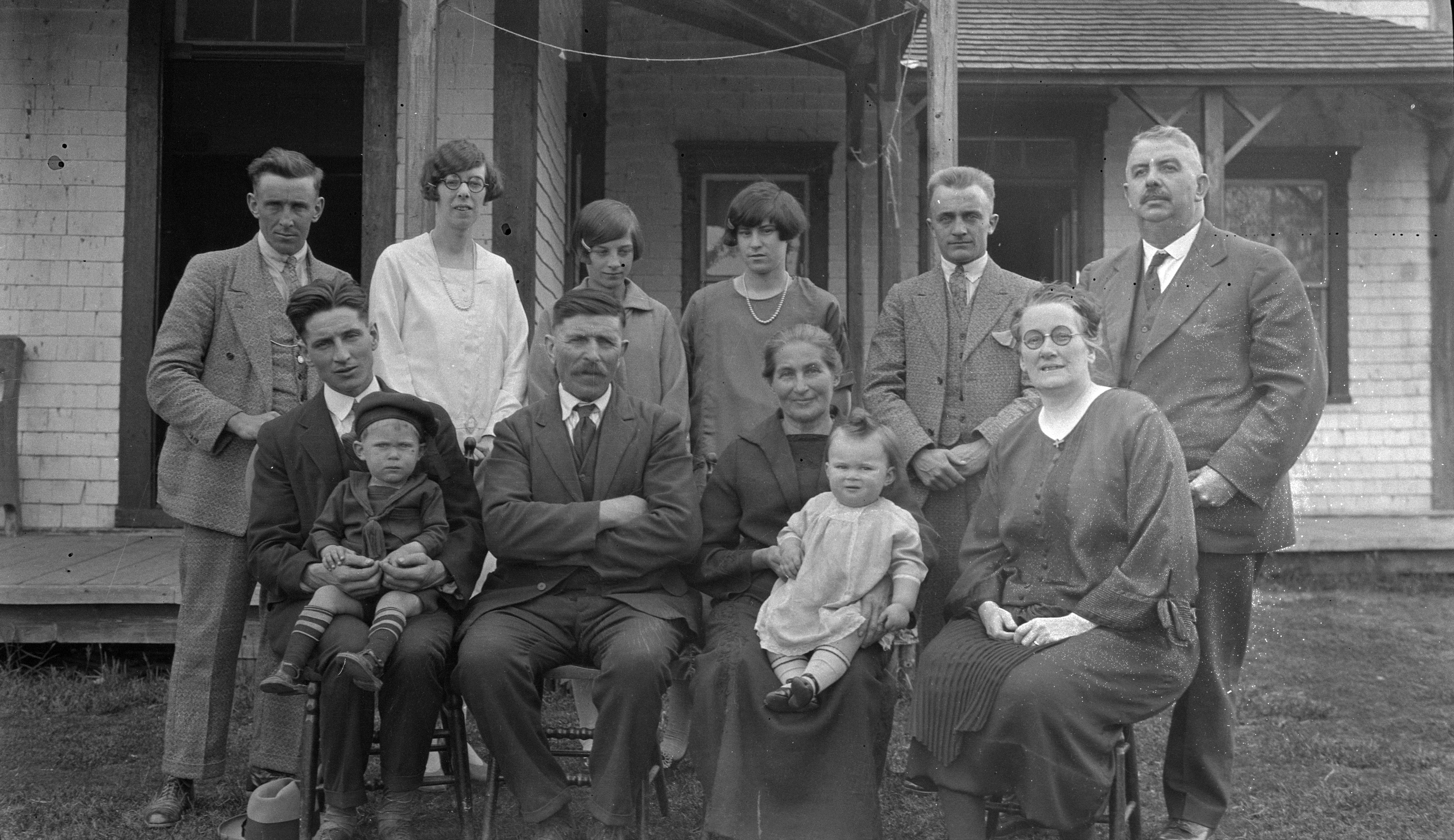 Photographie en noir et blanc d'une famille de 12 personnes placées sur deux rangées. Quatre personnes sont assises. Deux d'entre elles sont sur leur cuisses un bambin. Les six autres personnes sont debout derrière les chaises. 
