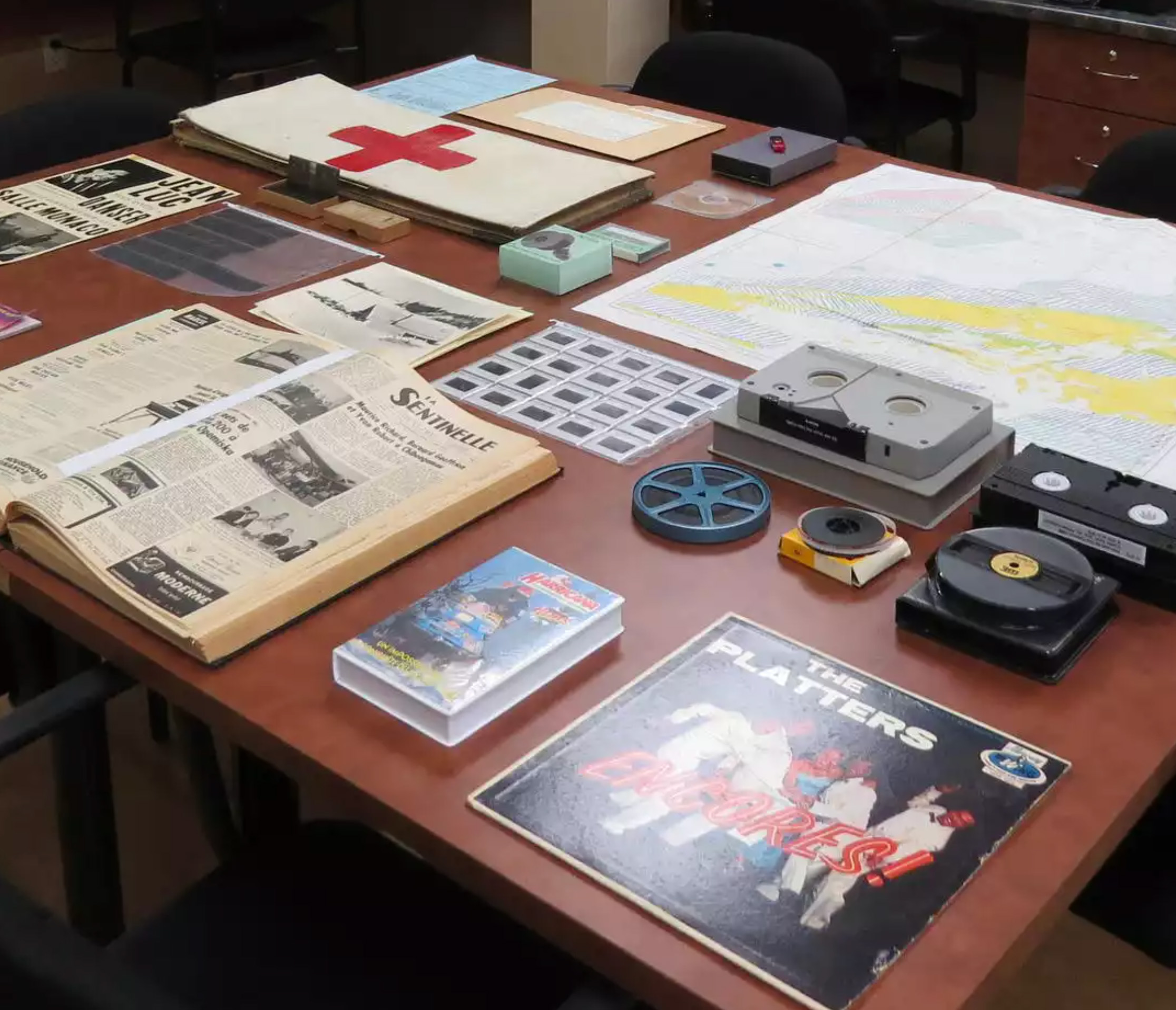 Des archives (diapositives, bandes magnétiques, négatifs, imprimés) exposés sur une table 