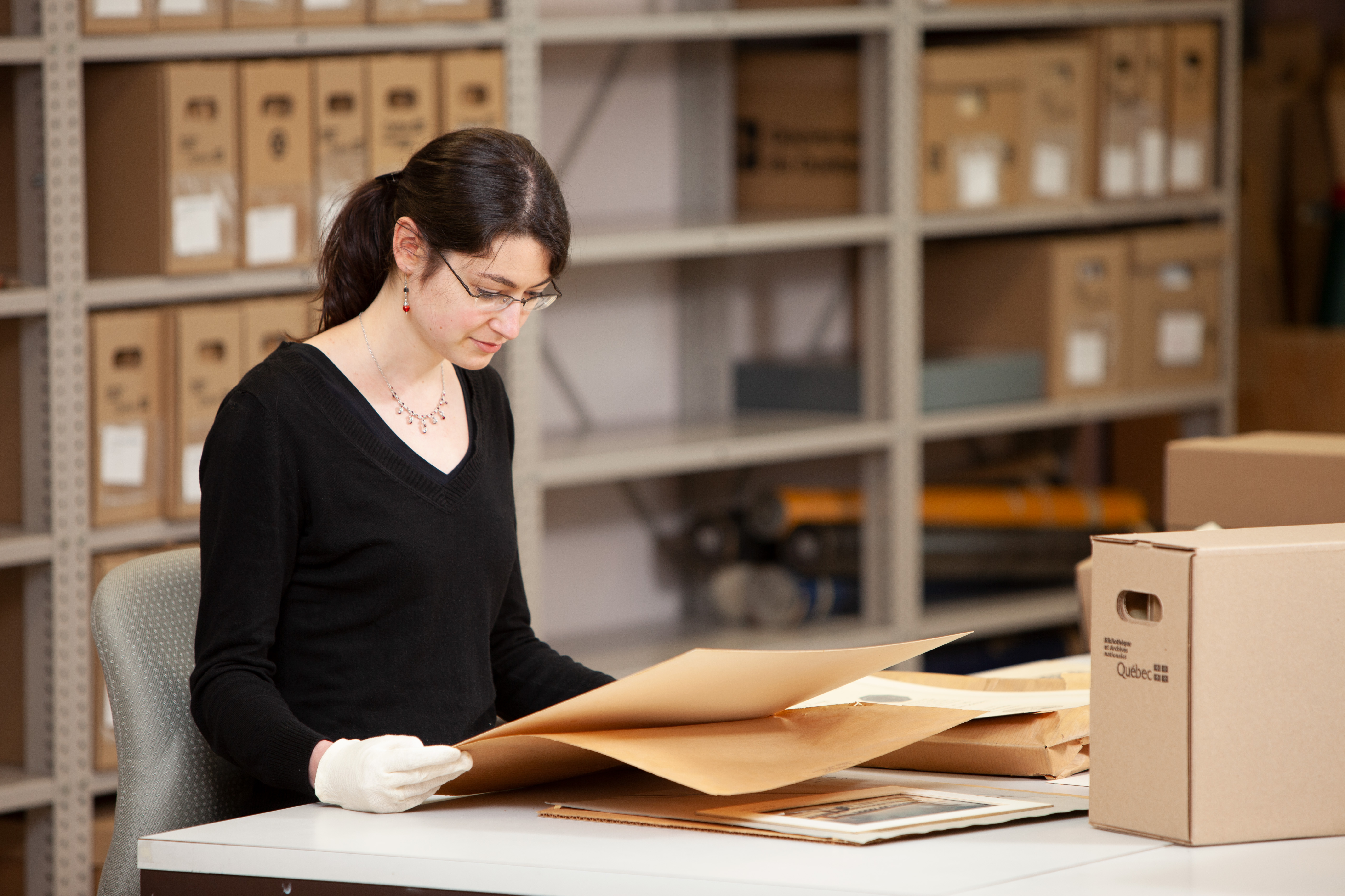 Employée des Archives nationales, entourée de boîtes d'archives, consultant des documents d'archives.