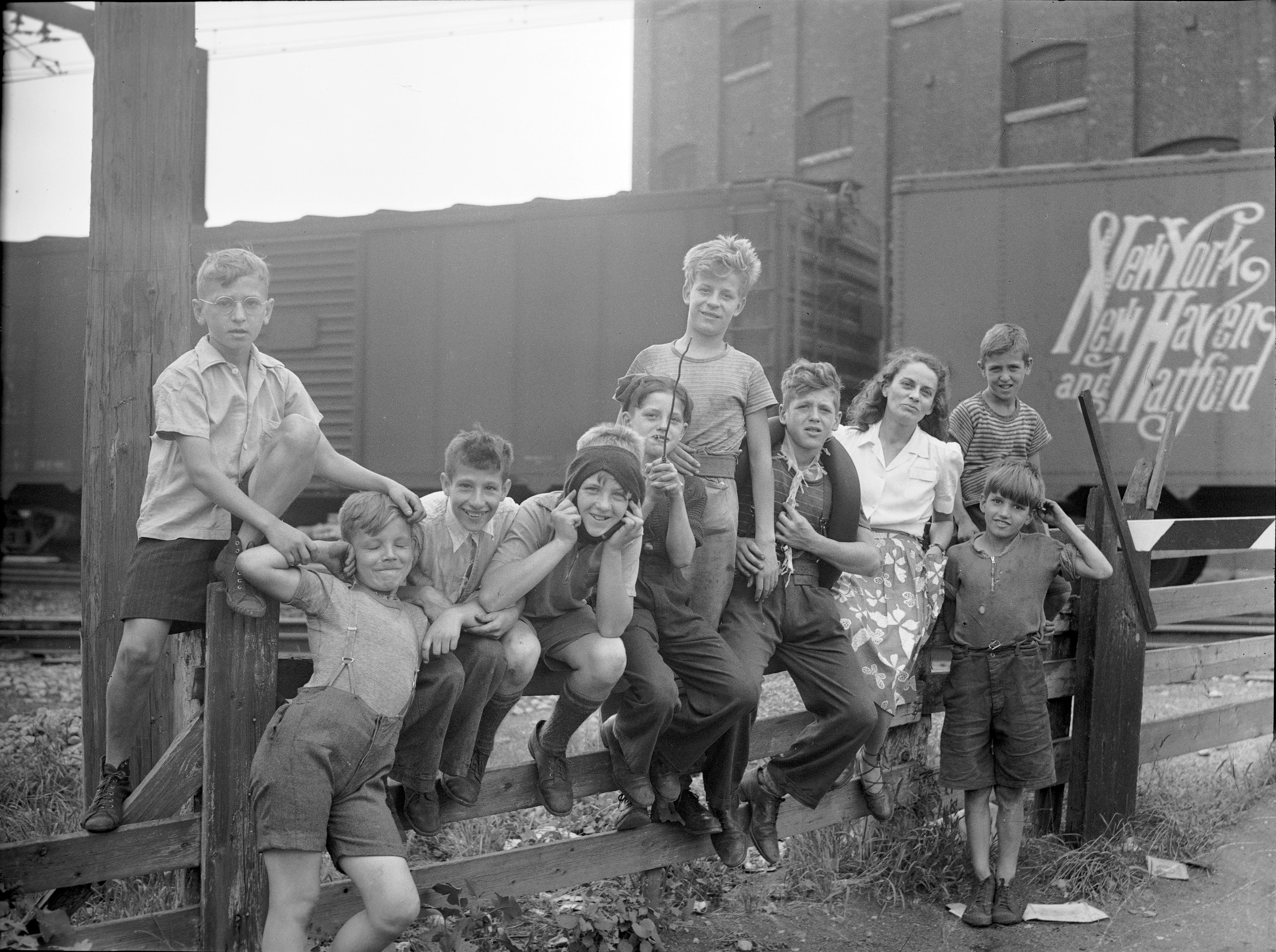 Gabrielle Roy entourée d'enfants dans le quartier Saint-Henri à Montréal. En arrière-plan des wagons de marchandise