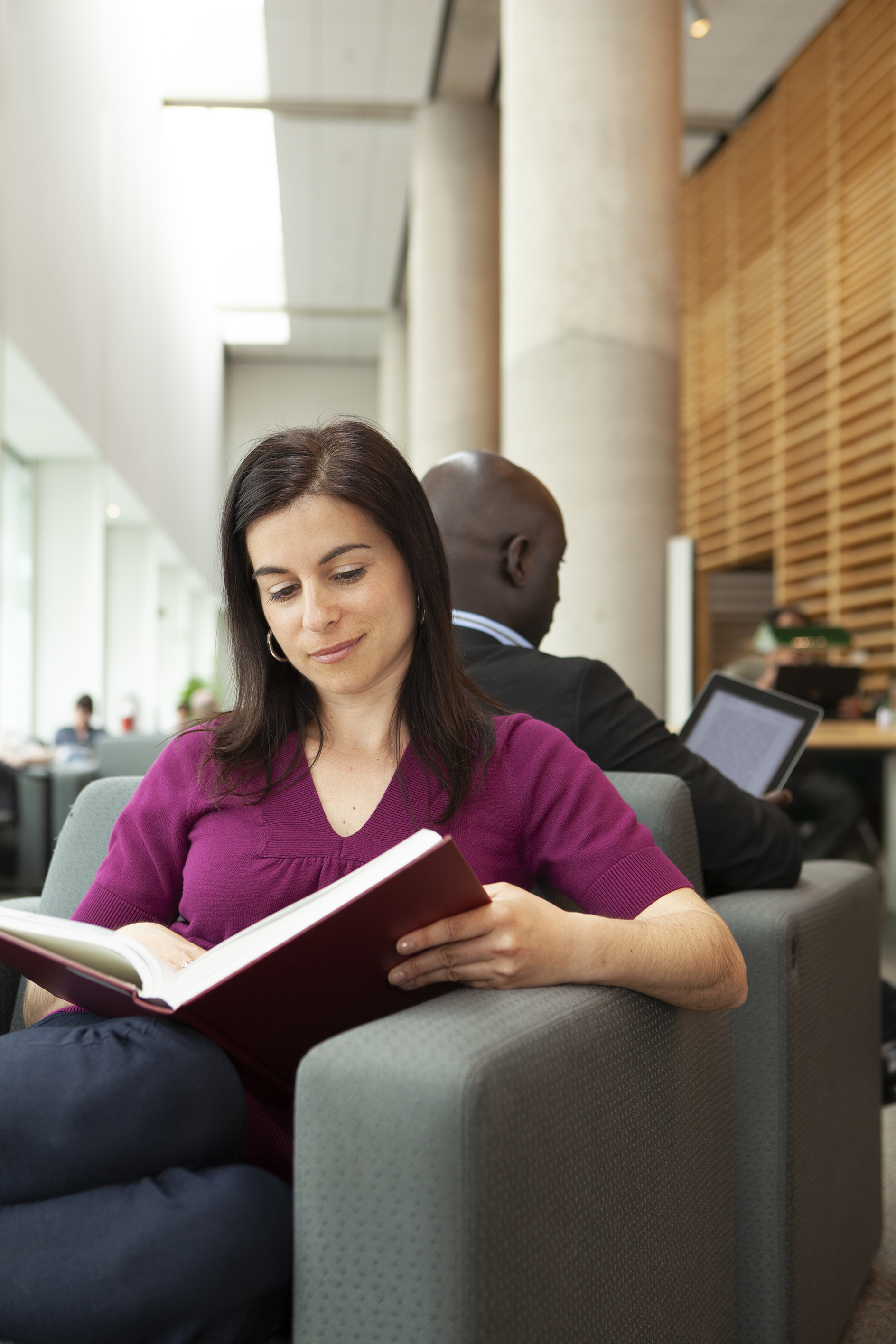 Une femme lisant un livre papier. Lui faisant dos, un homme lit sur une tablette numérique.