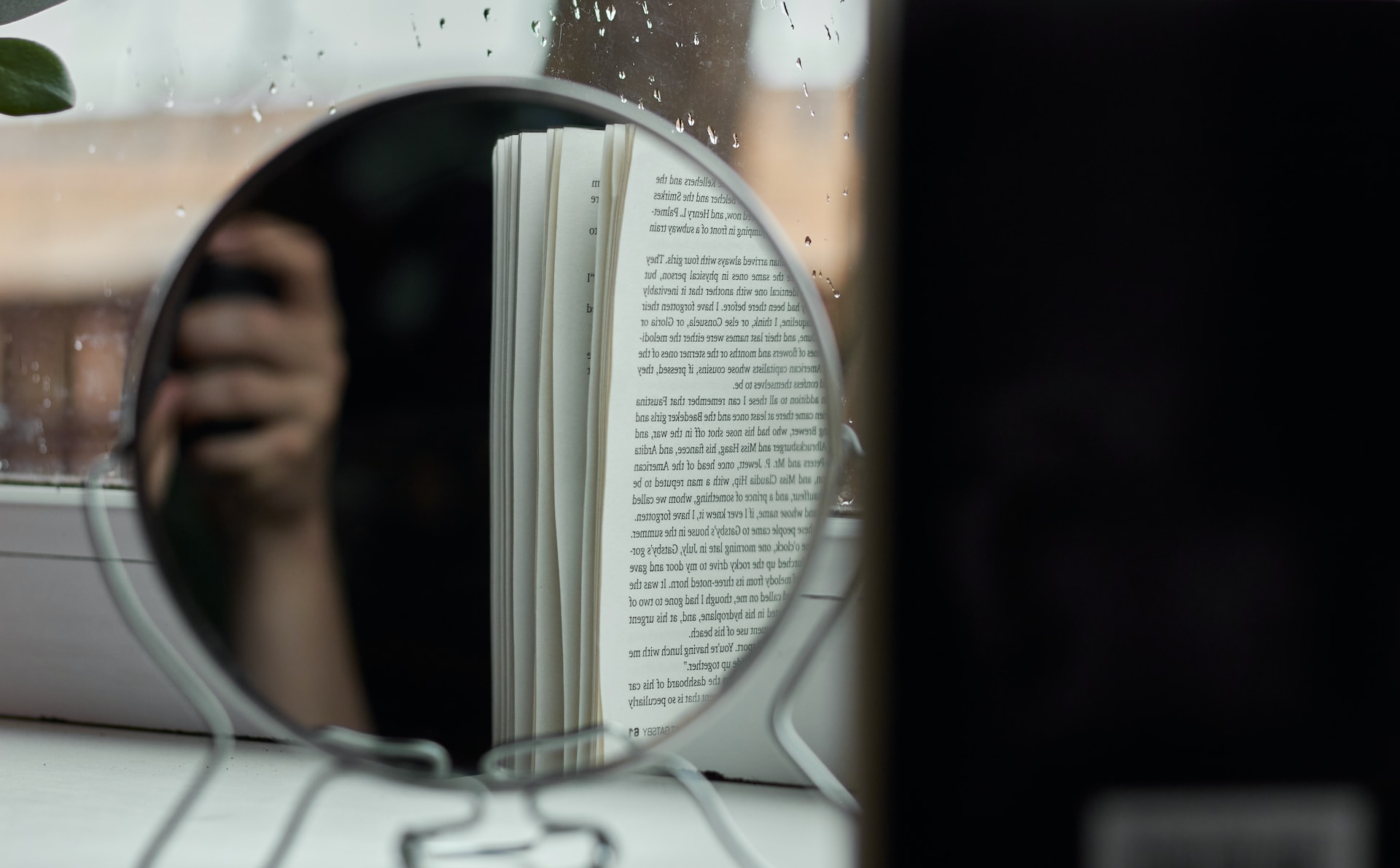 Reflet d'une main et d'un livre dans un miroir de table.