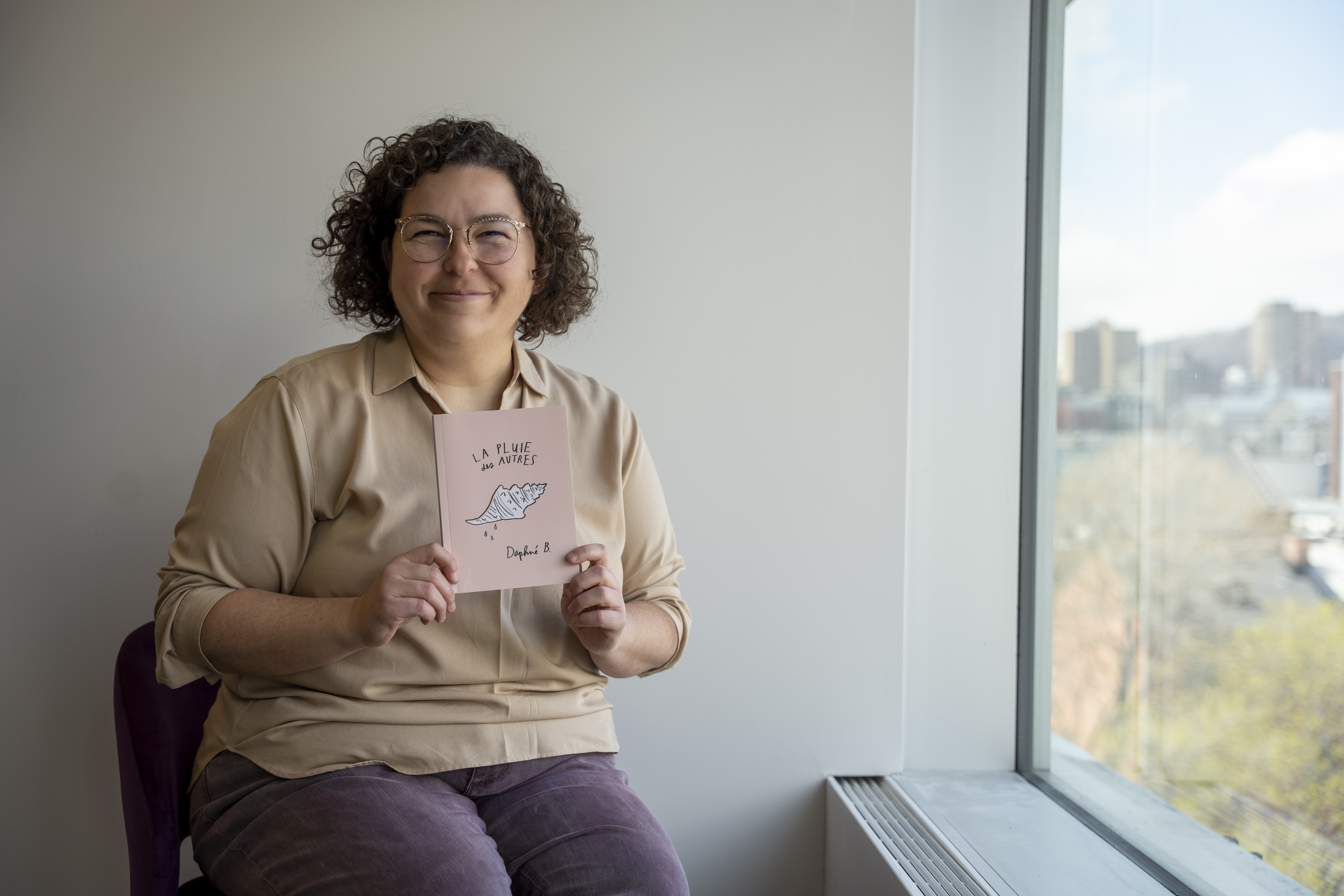 Jeune femme souriante tenant le livre La pluie des autres, de Daphné B.