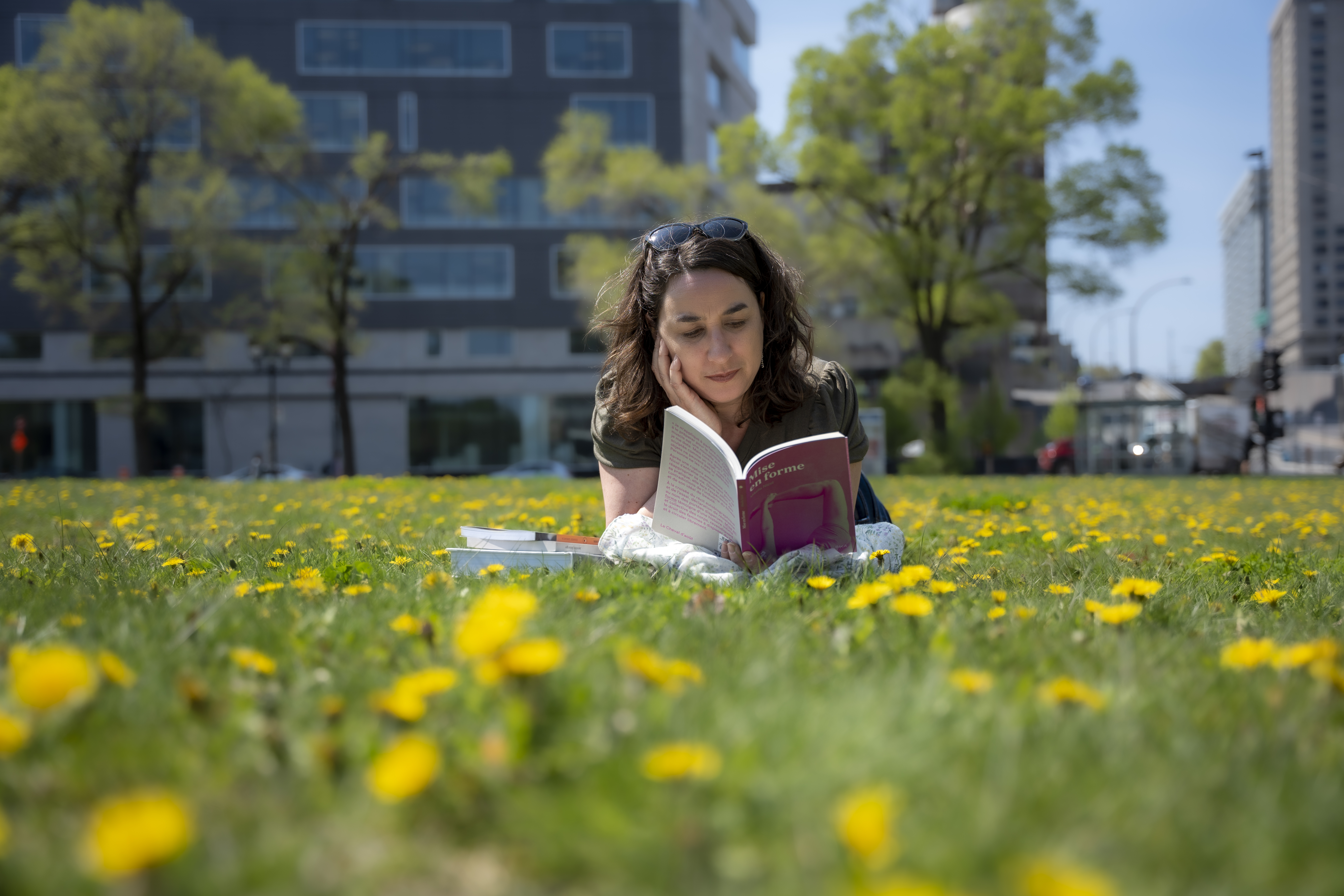 Femme couchée dans l'herbe et les pissenlits lit un livre.