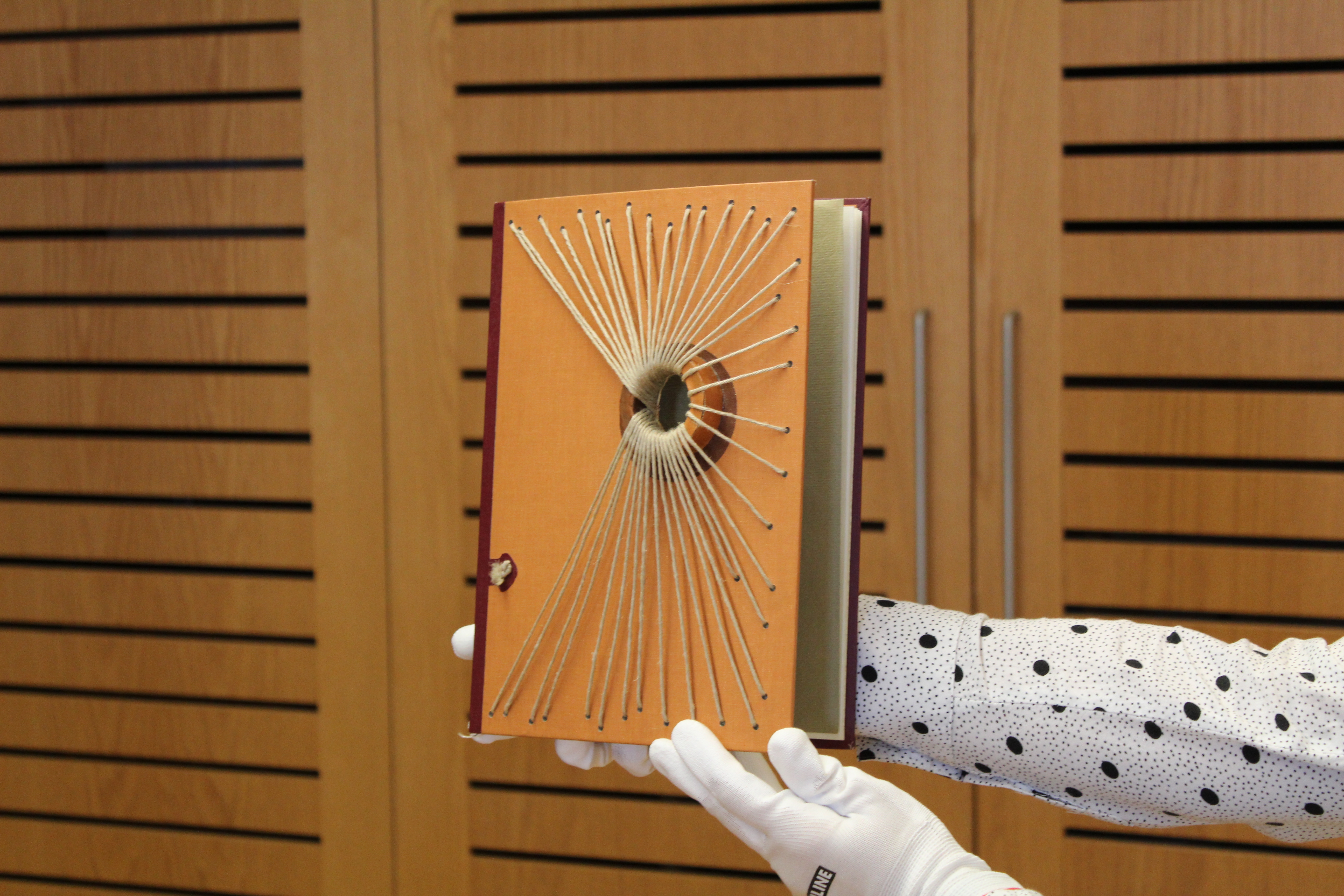 Photographie d'une reliure de Gabriel Rivard. La reliure se particularise par le trou en son centre duquel sont attachées des ficelles, elles mêmes fixées tout autour de la couverture.