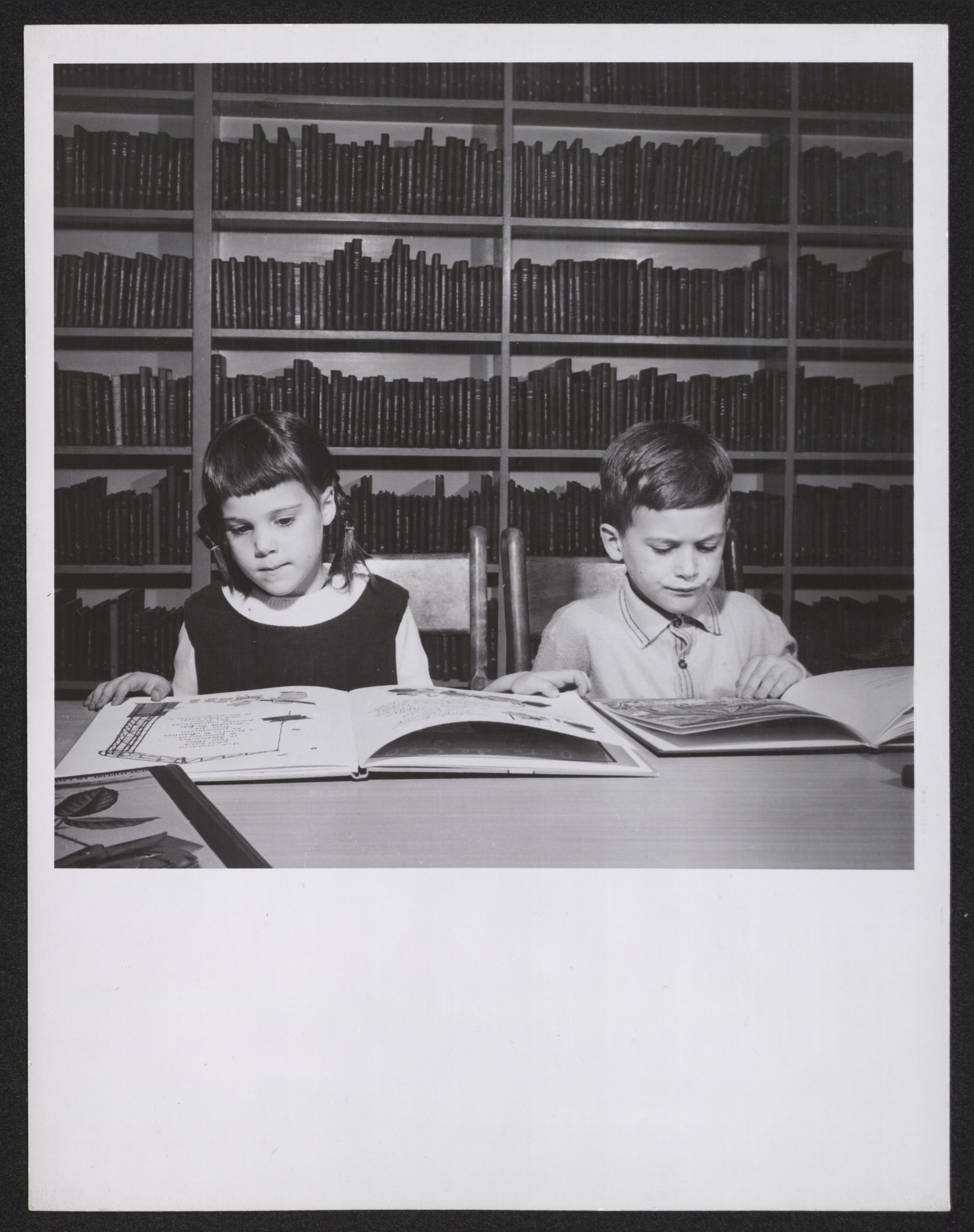 Un garçon et une fille lisent respectivement un livre, assis à une table à la bibliothèque.