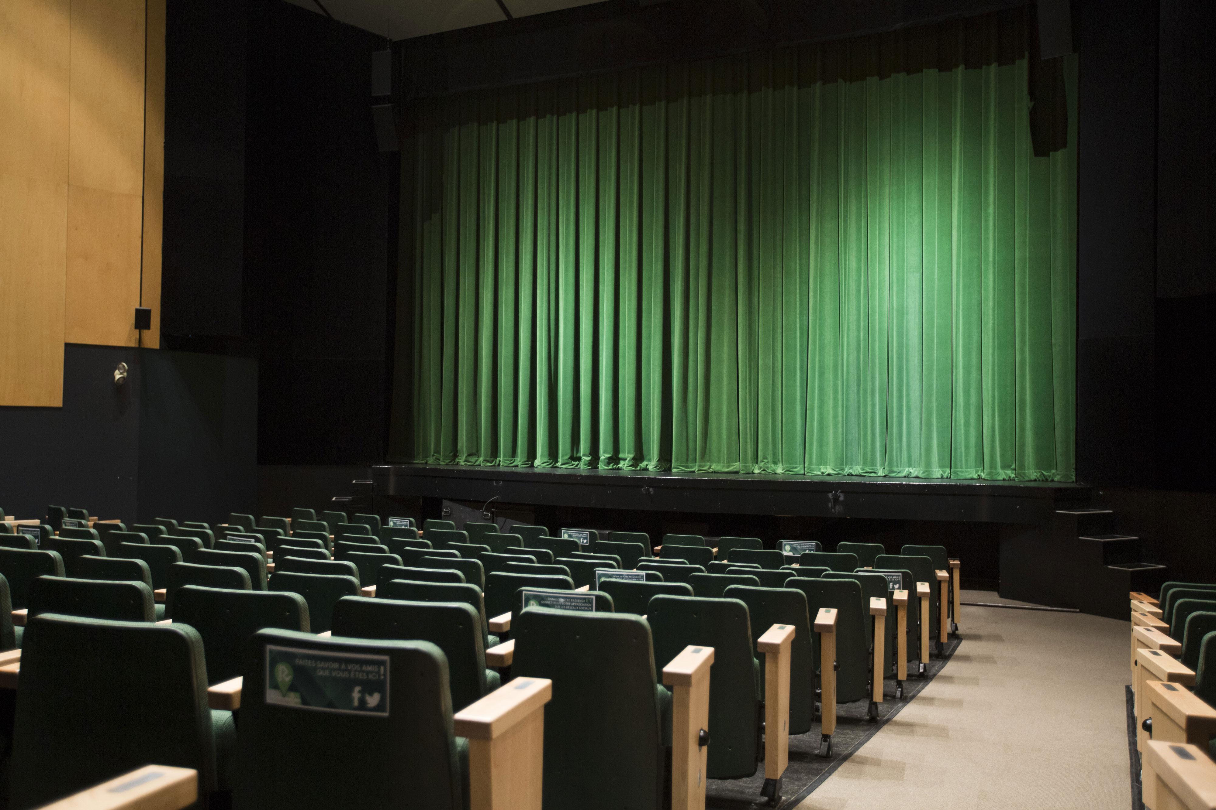 Salle de spectacle avec sièges et scène dotée d'un rideau vert.