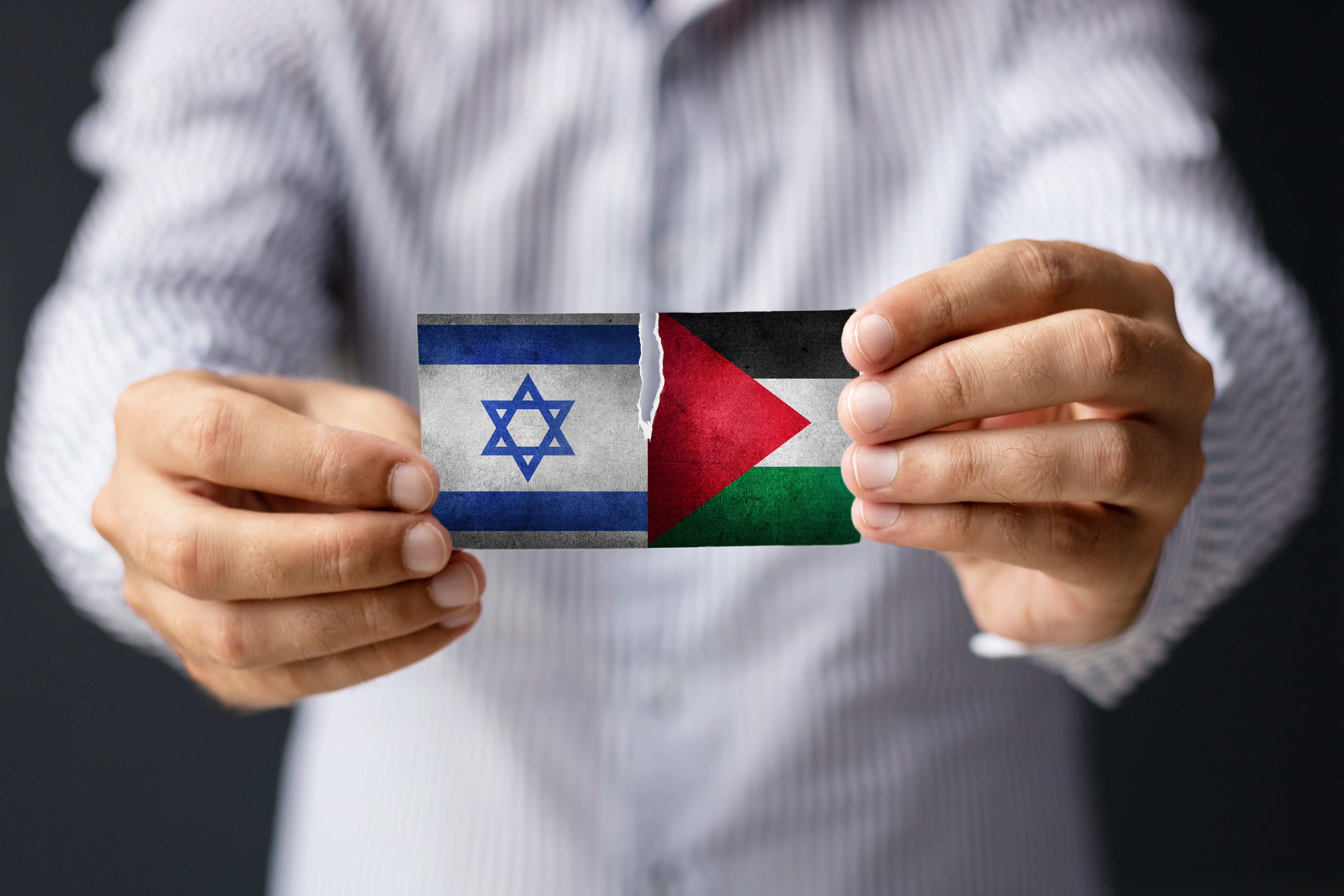 Un homme tient deux petits drapeaux partiellement déchirés. celui d'Israël et celui de la Palestine.