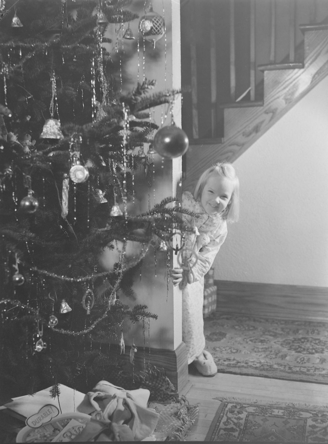 Une jeune fille se cache derrière un sapin de Noël.