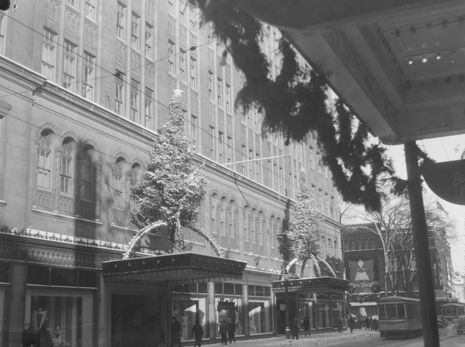 Nous voyons la façade du magasin à rayons Eaton's de la rue Sainte-Catherine Ouest à Montréal. Il y a un arbre de Noël sur les deux marquises des portes d'entrée.