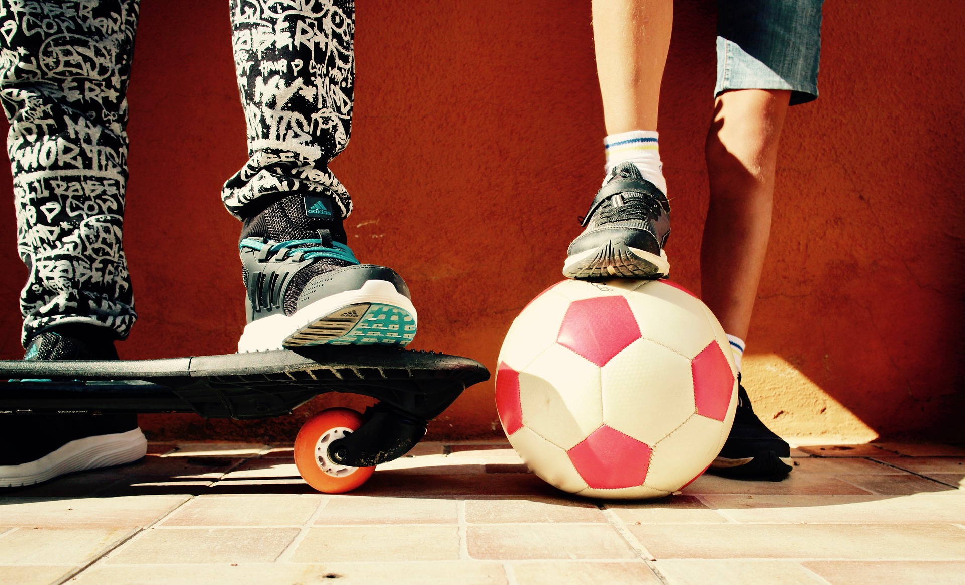 Pieds d'un enfant sur une planche à roulettes. Pieds d'un autre enfant à côté de ballon de soccer.