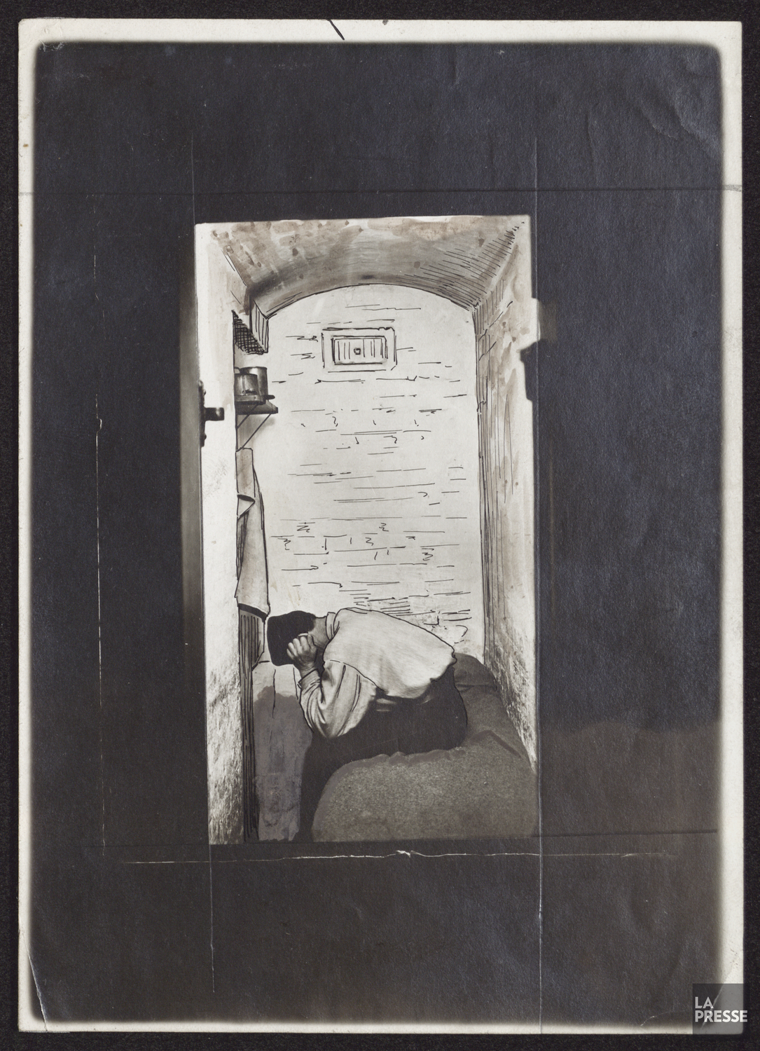 Un homme pose la tête sur ses genoux, assis sur un lit dans une cellule de prison. 