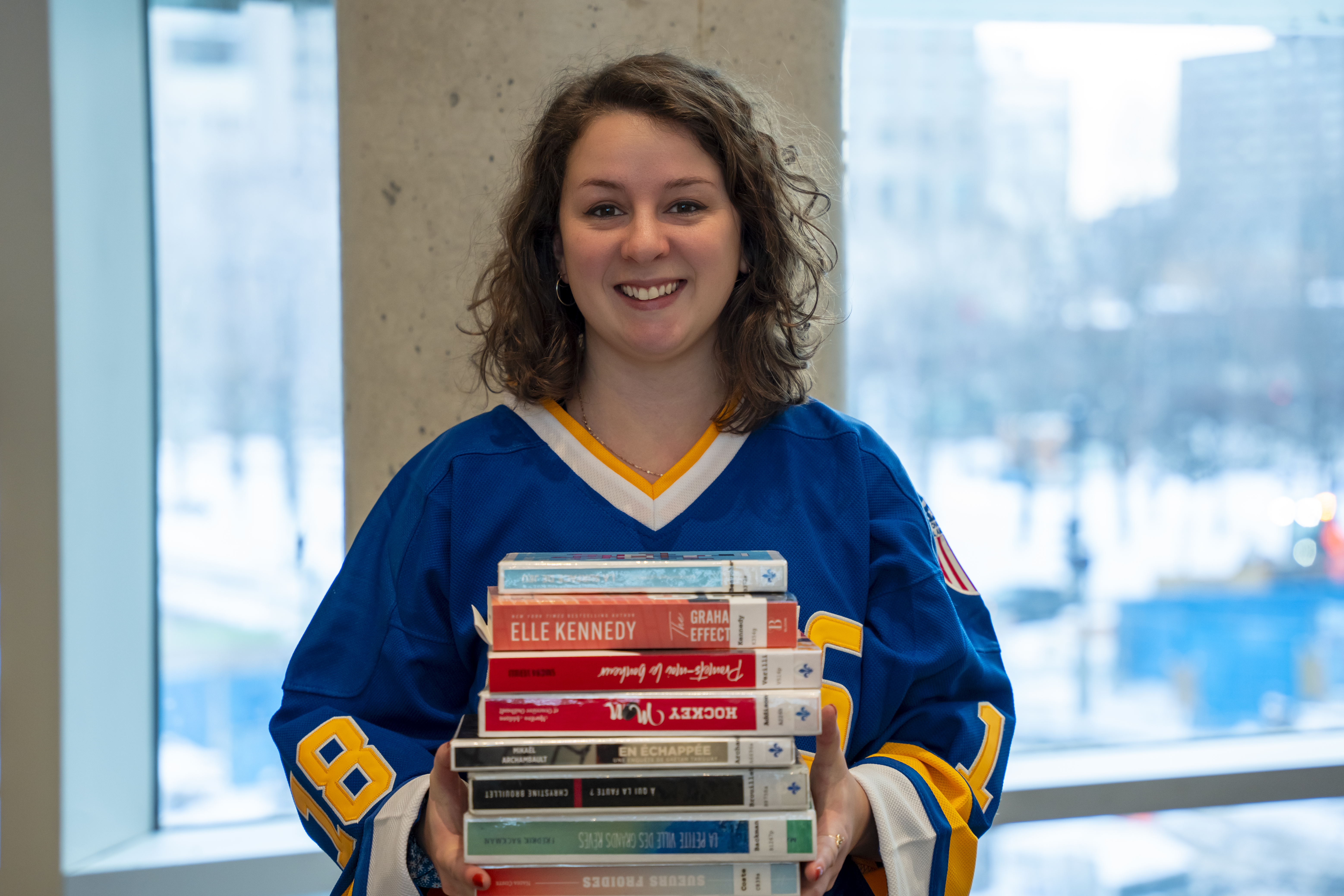 Une jeune femme portant un chandail de hockey tient une pile de livres dans ses mains.