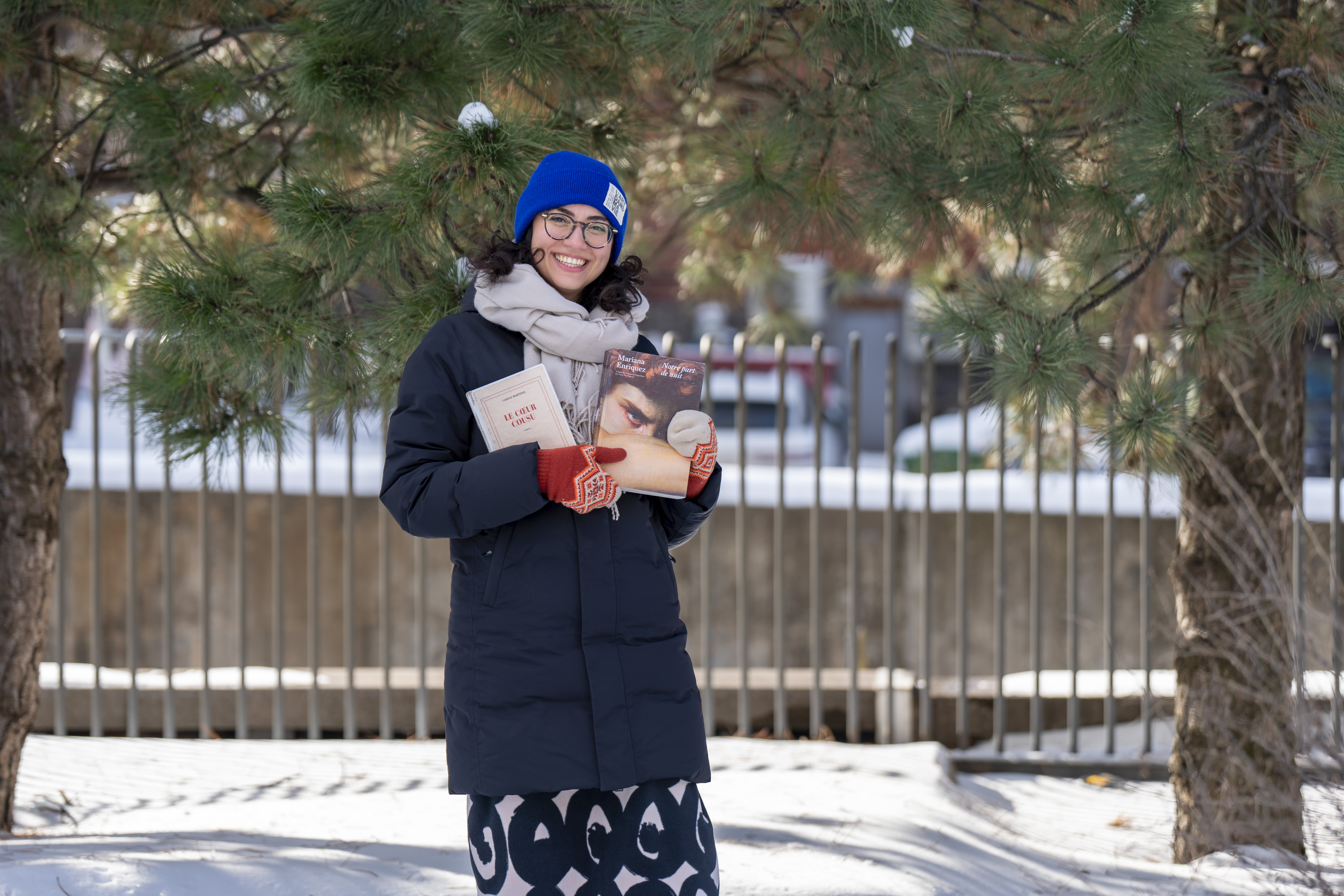 Une femme souriant tient des livres, dehors en hiver.