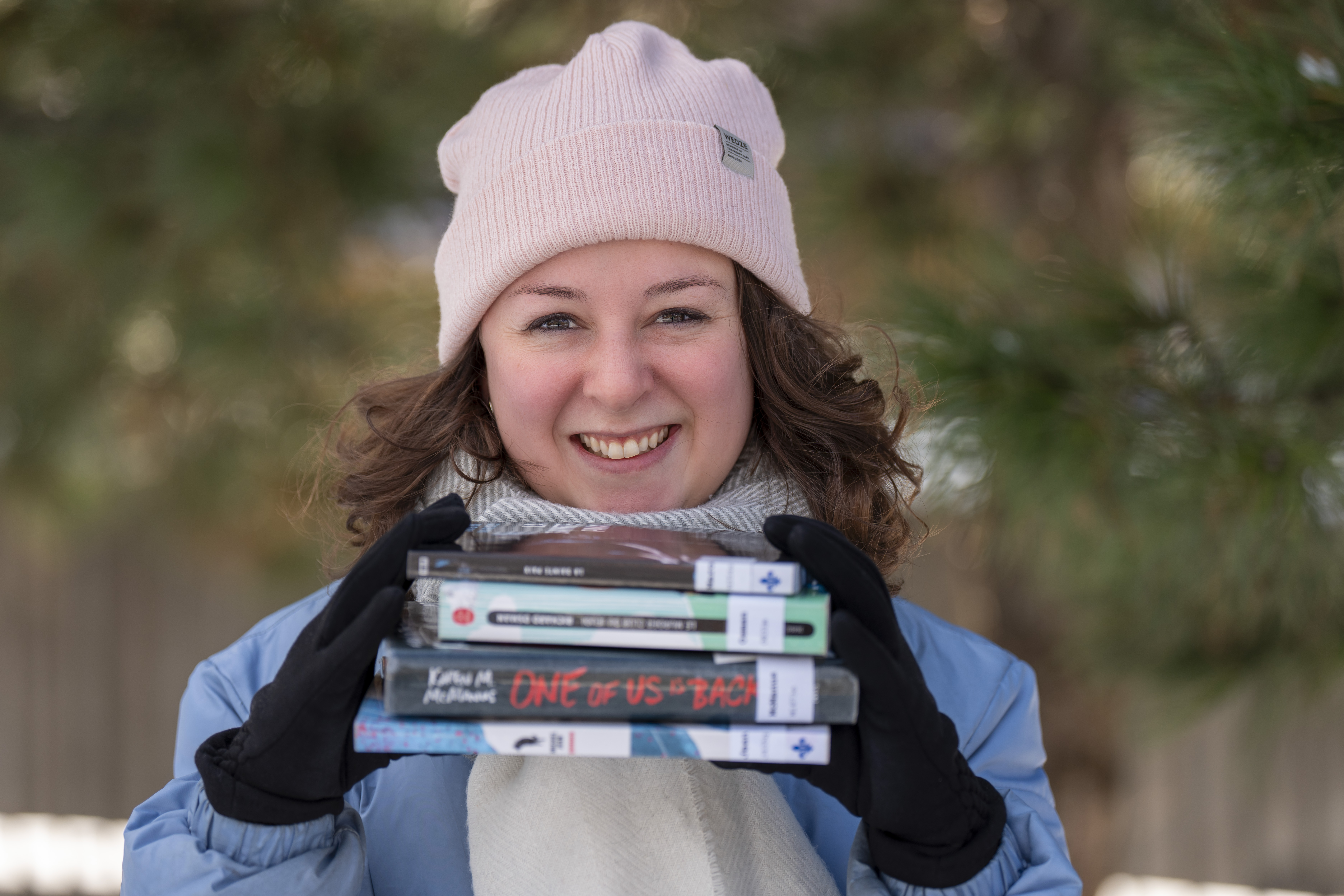 Jeune femme souriante portant un tuque et des gants tient une pile de quatre livres.