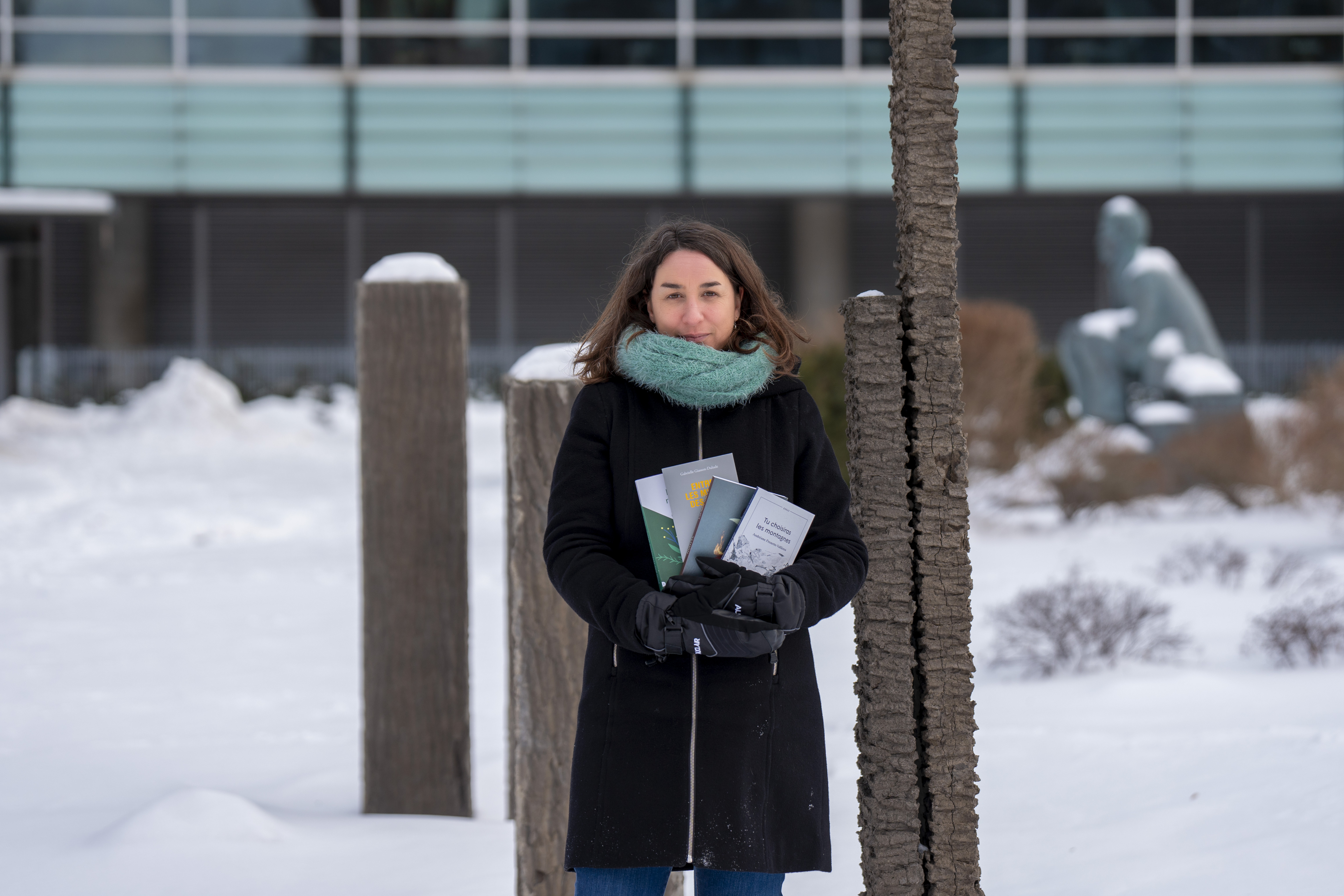 Une femme tient des livres devant une sculpture, en hiver.