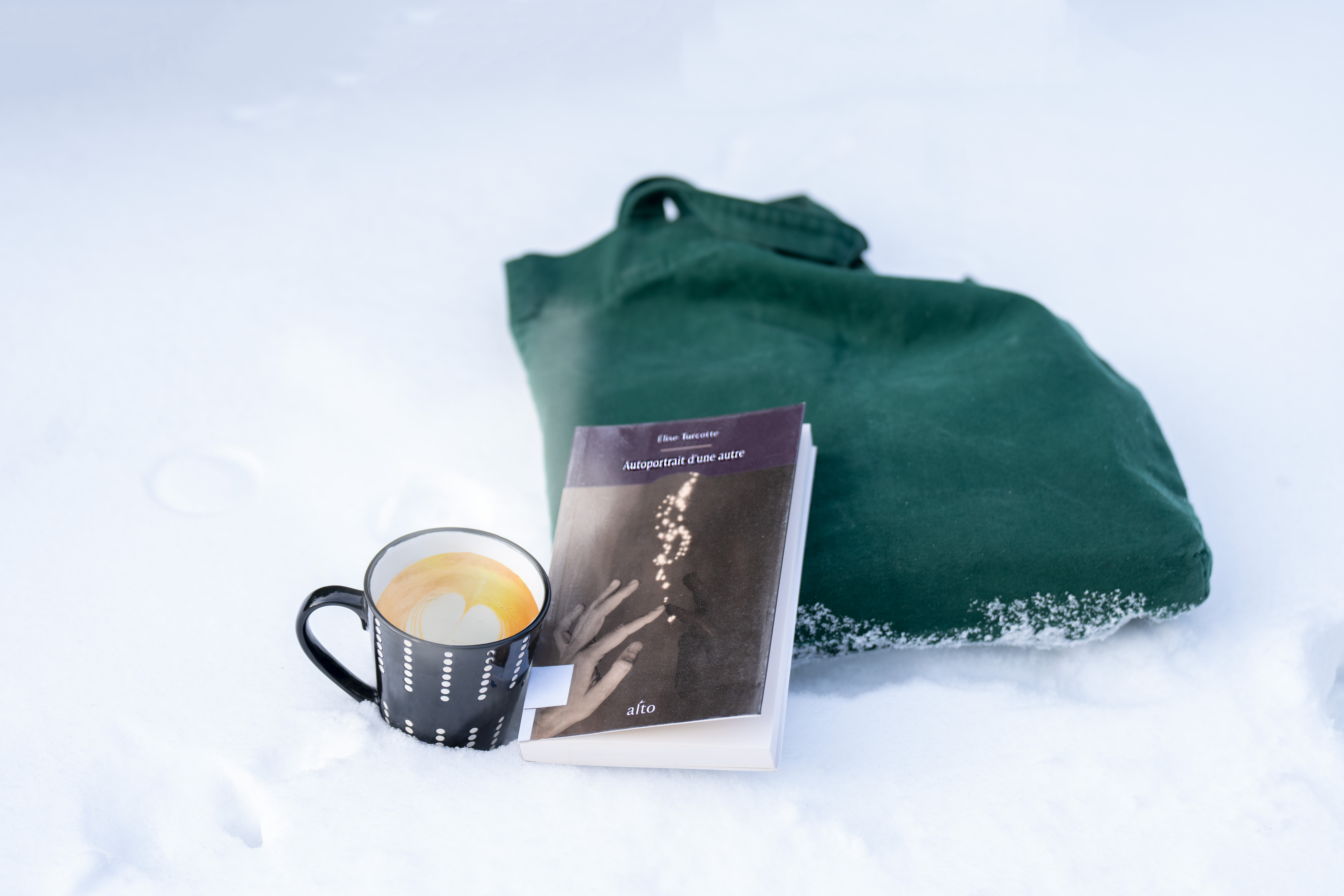 Un sac, une tasse de café et le livre "Autoportrait d'une autre" d'Élise Turcotte dans la neige.