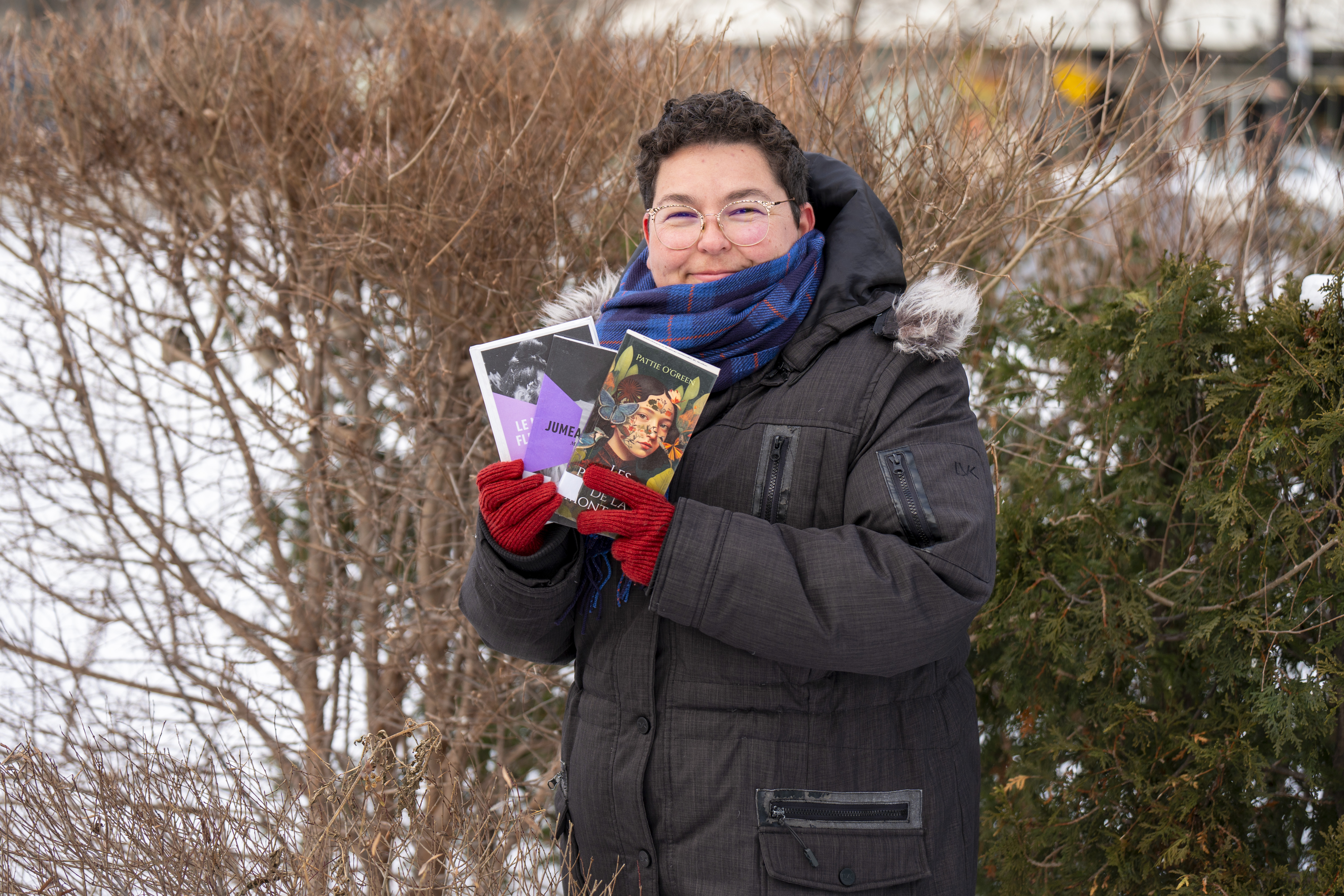 Femme souriant tenant des livres, dehors en hiver.