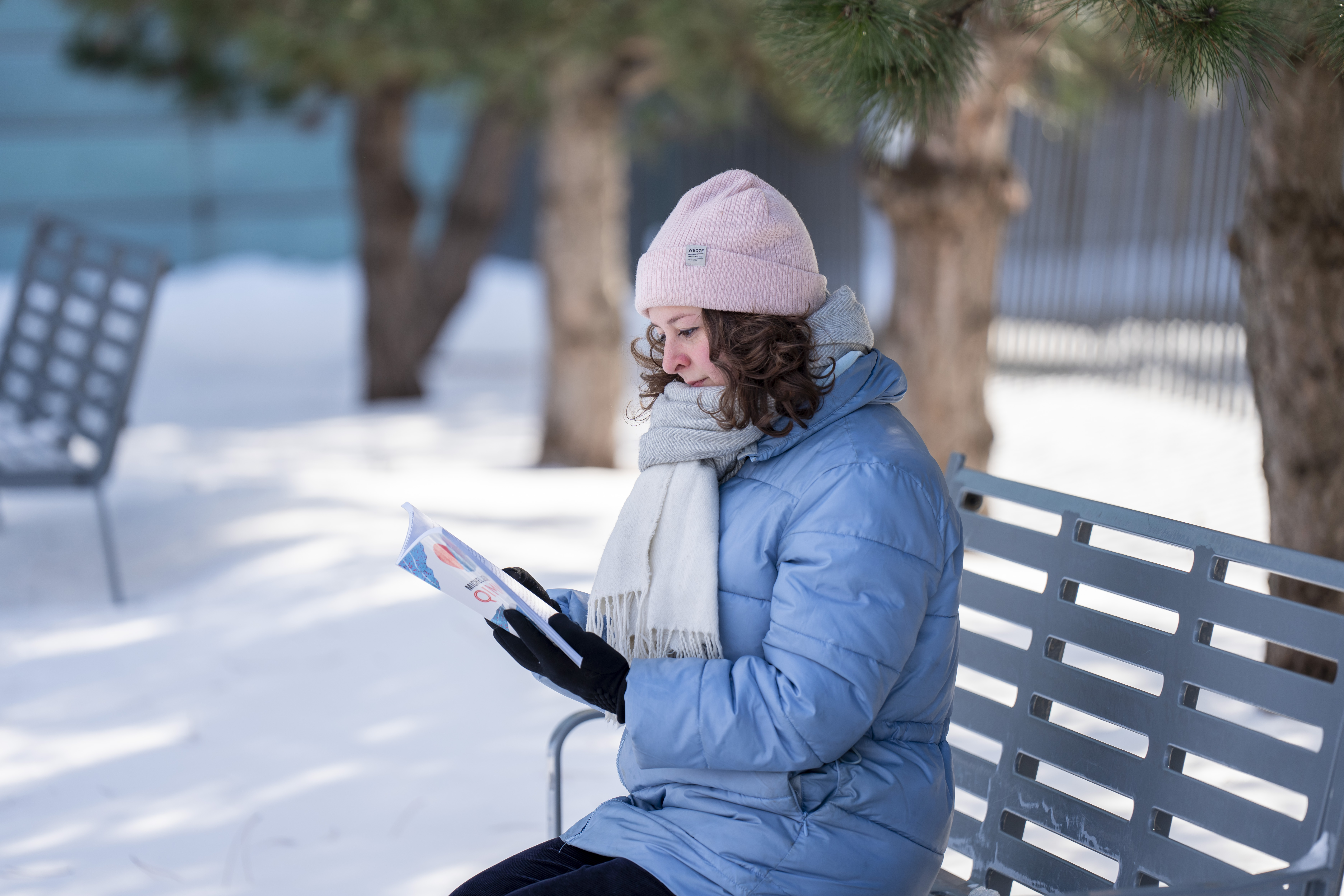 Une femme lit un livre sur un banc dans la neige.