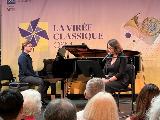 Durant la Virée Classique de l'OSM, un homme est assis à un piano à queue tandis qu'une femme assise devant un lutrin parle dans un micro.