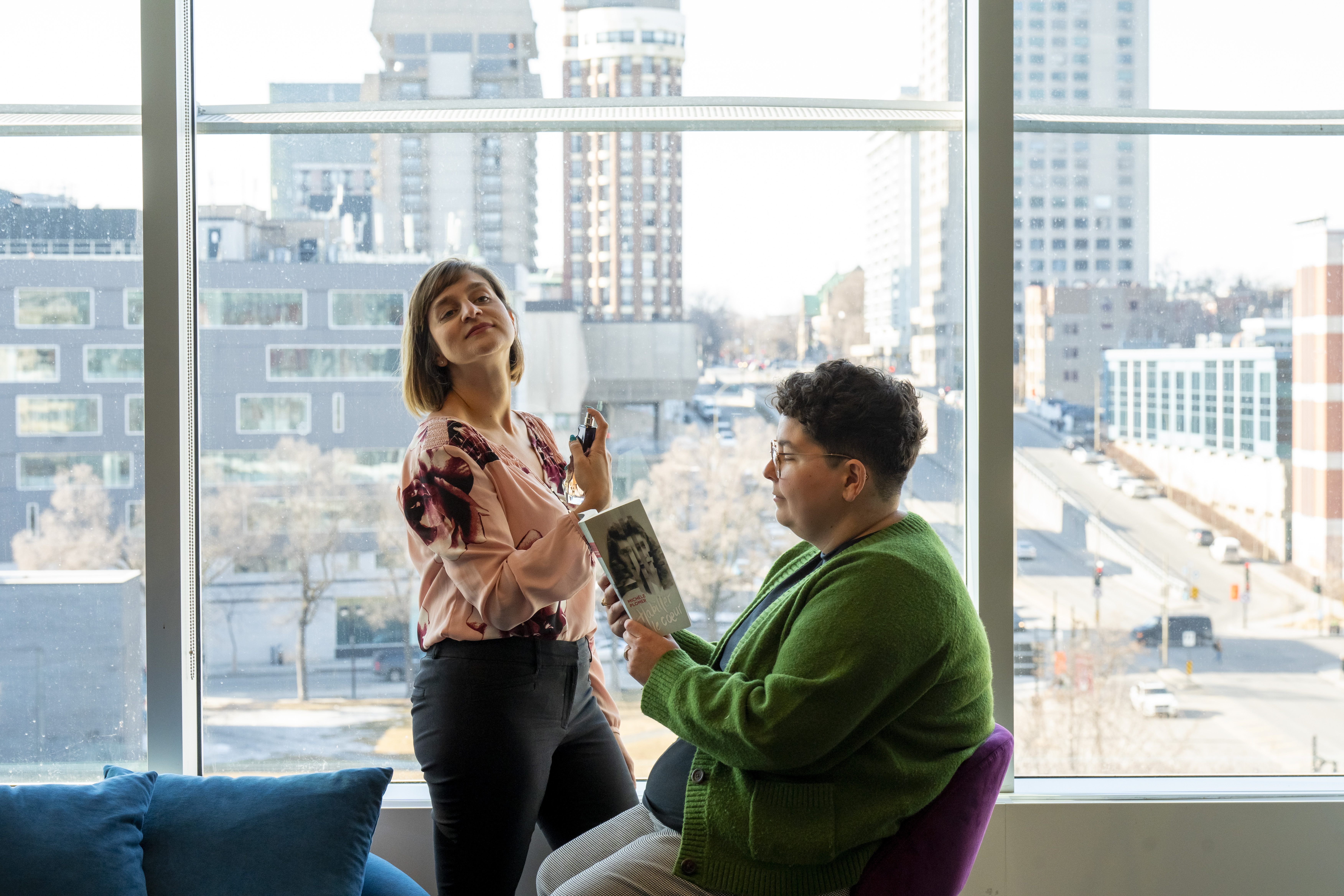 Une femme se parfume tandis qu'une autre lit un livre.