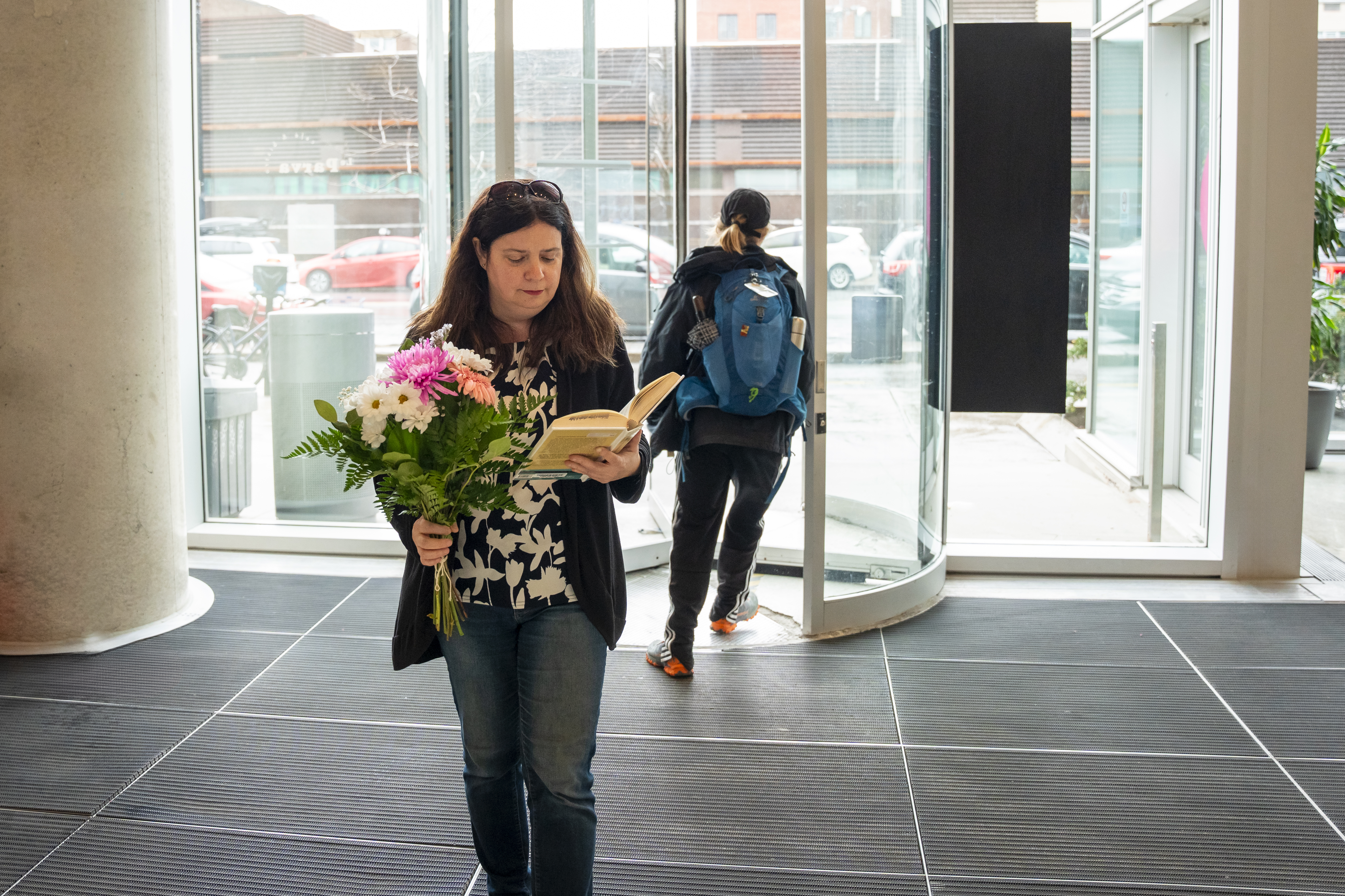 Femme lisant une livre, fleurs à la main, devant une porte tournante.