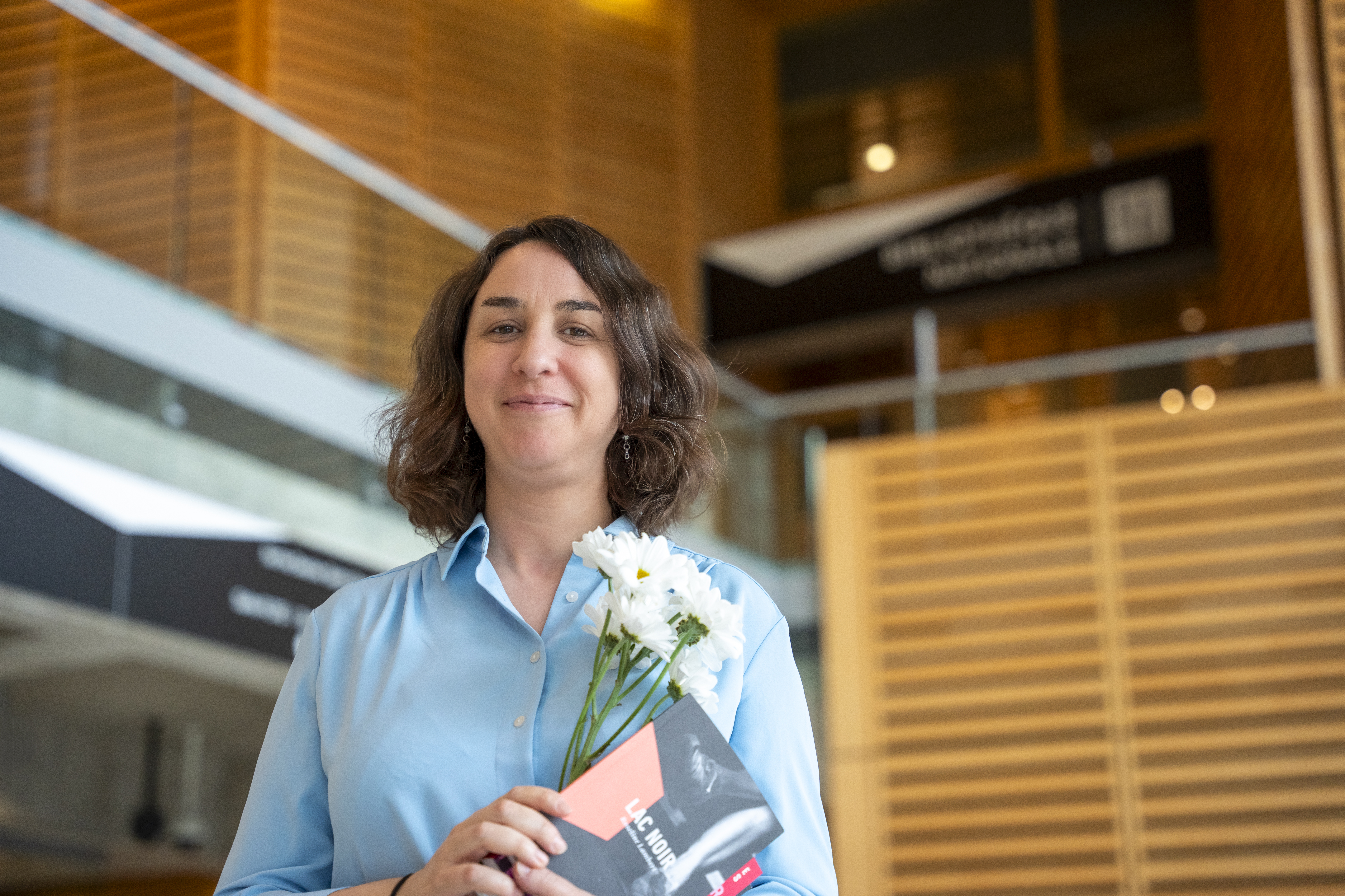 Femme tenant un livre et des marguerites à la Grande Bibliothèque.
