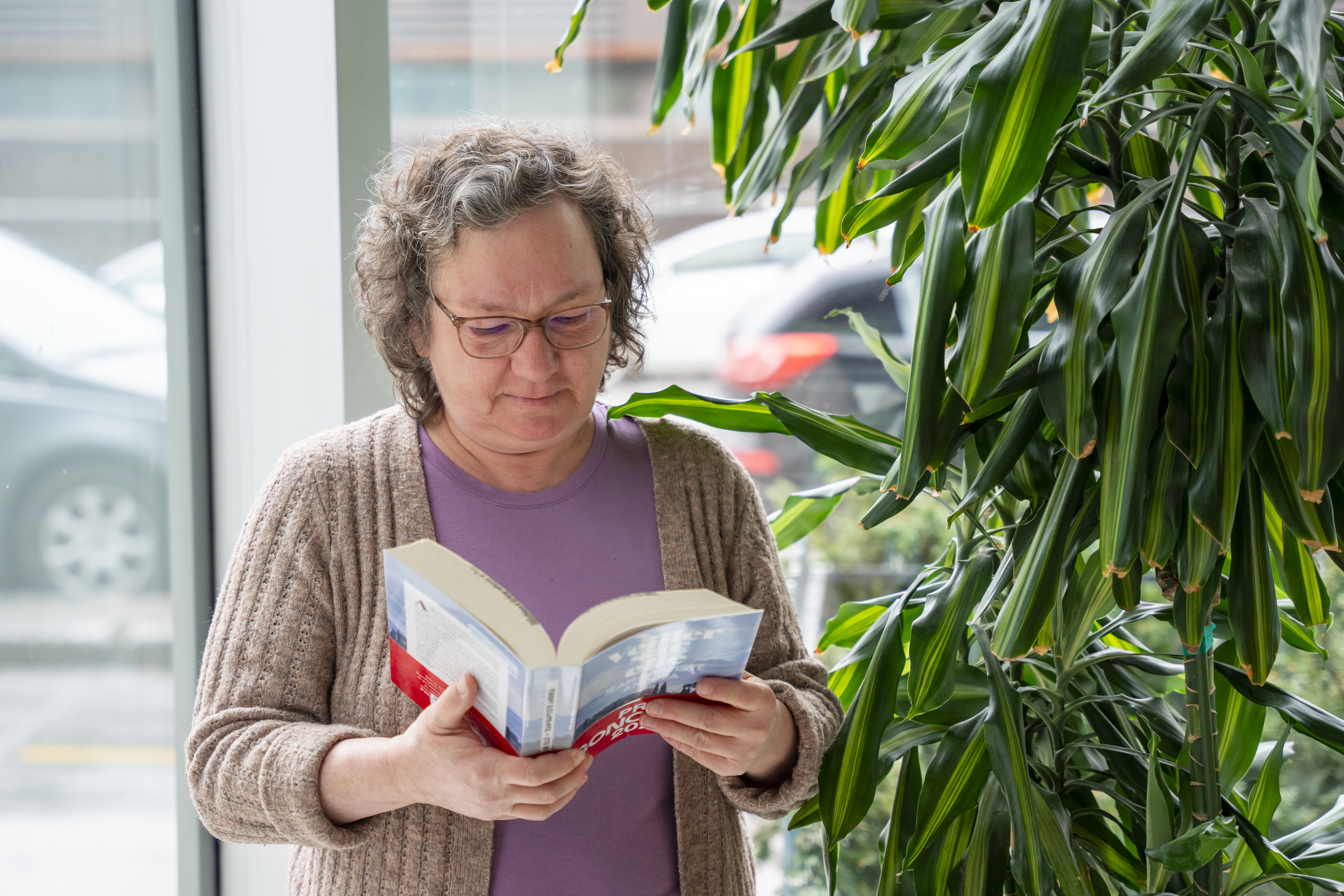 Femme lisant un livre près d'une grande plante.
