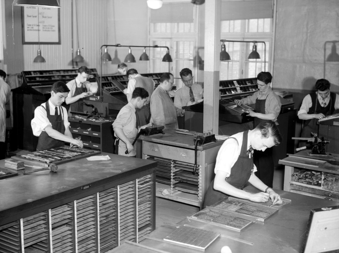 On aperçoit plusieurs jeunes hommes s'exerçant au métier de typographe. 