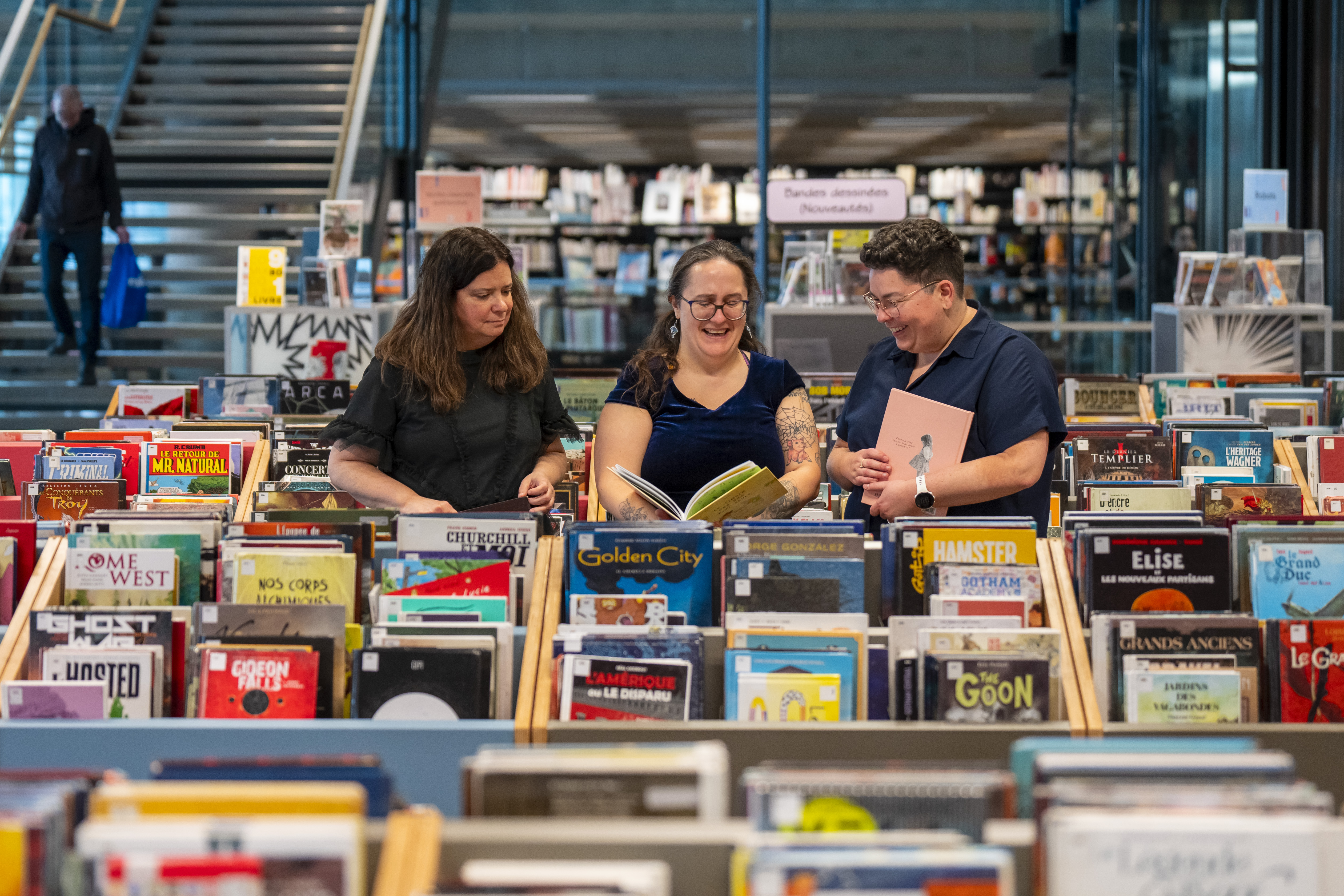 Trois femmes entourées de bacs remplis de bandes dessinées.