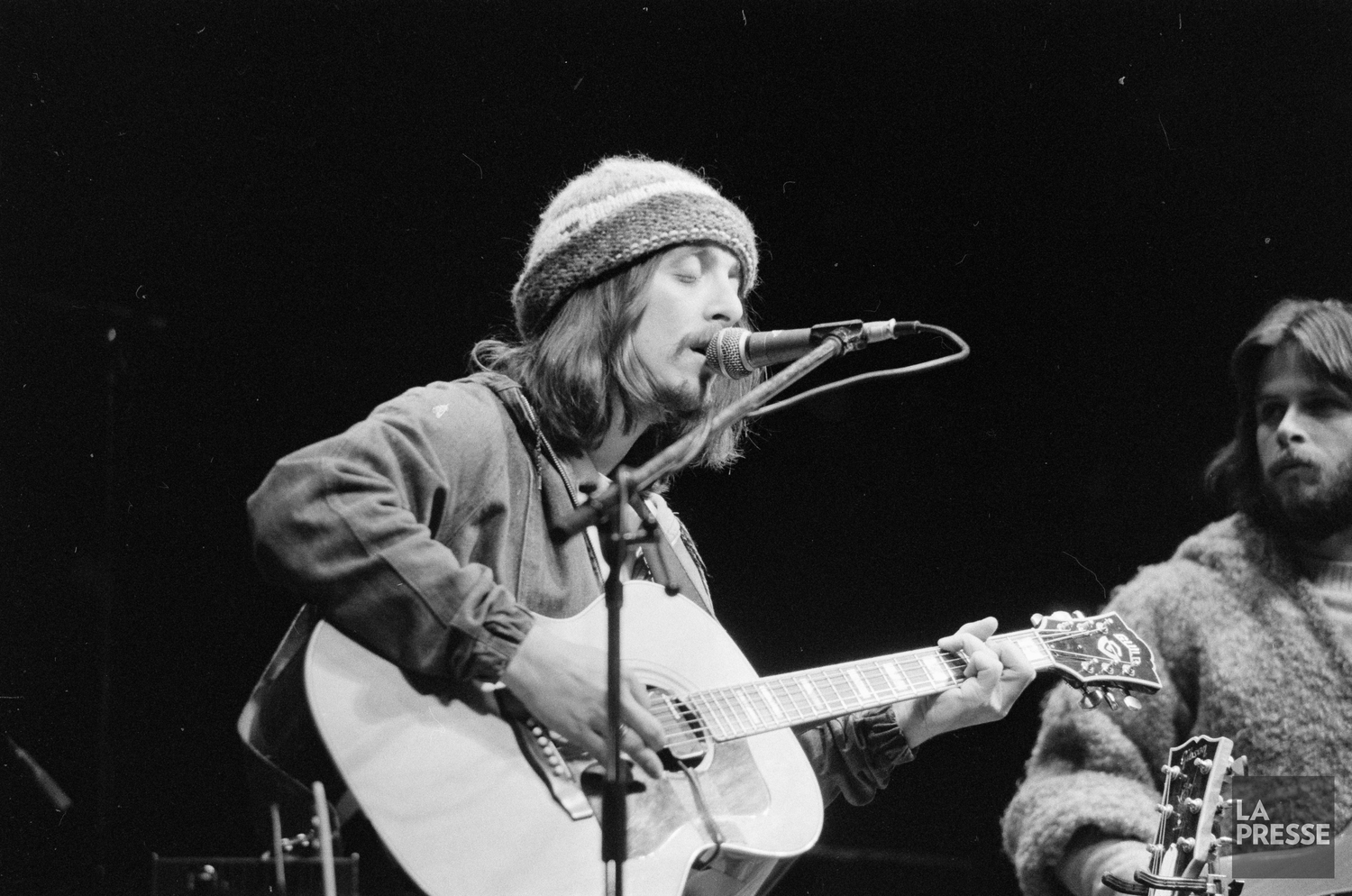 Serge Fiori chante et joue de la guitare tandis que Louis Valois, à ses côtés, le regarde. en concert
