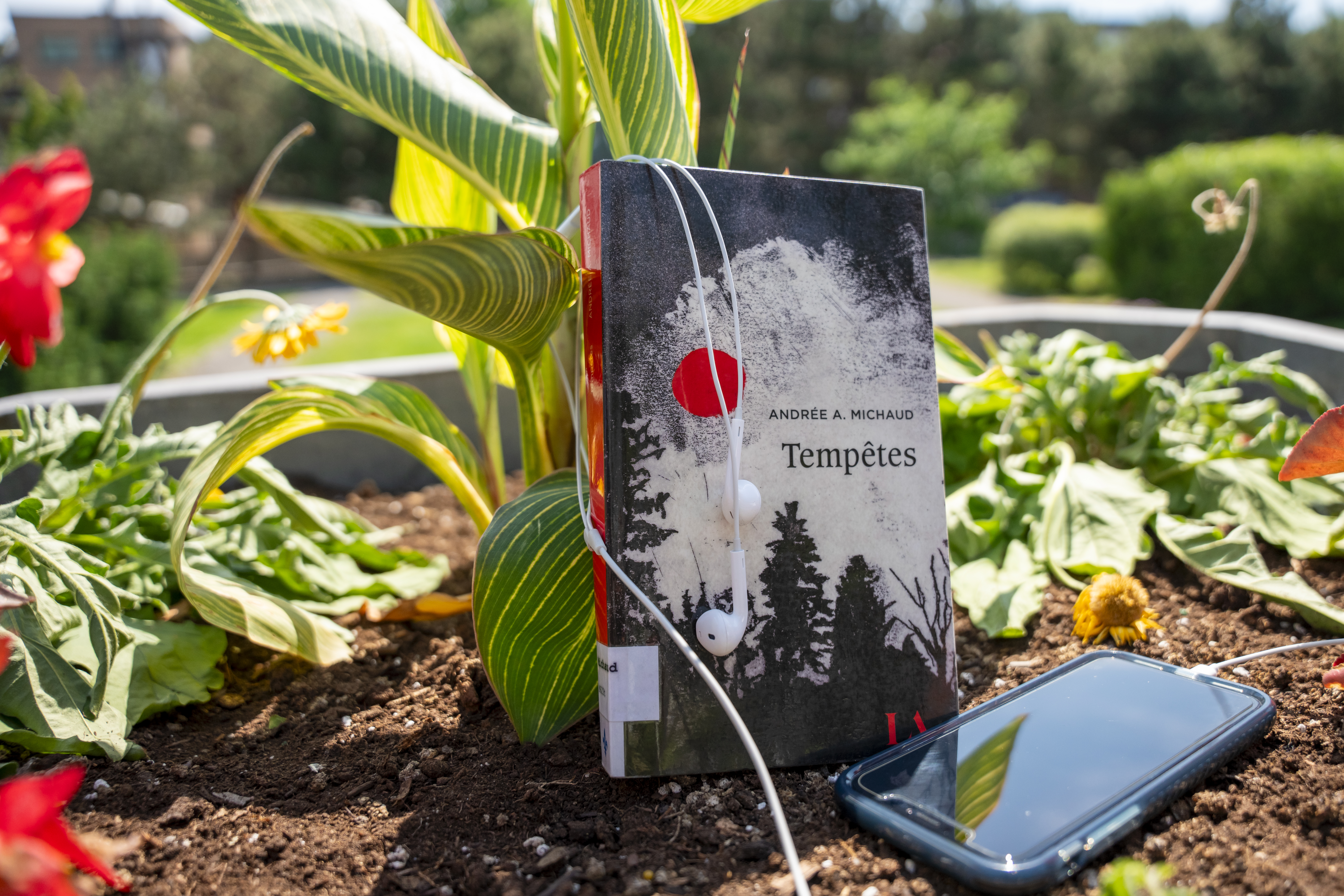 Parmi les plantes, le livre Tempêtes d'Andrée A. Michaud et un téléphone cellulaire avec des écouteurs.