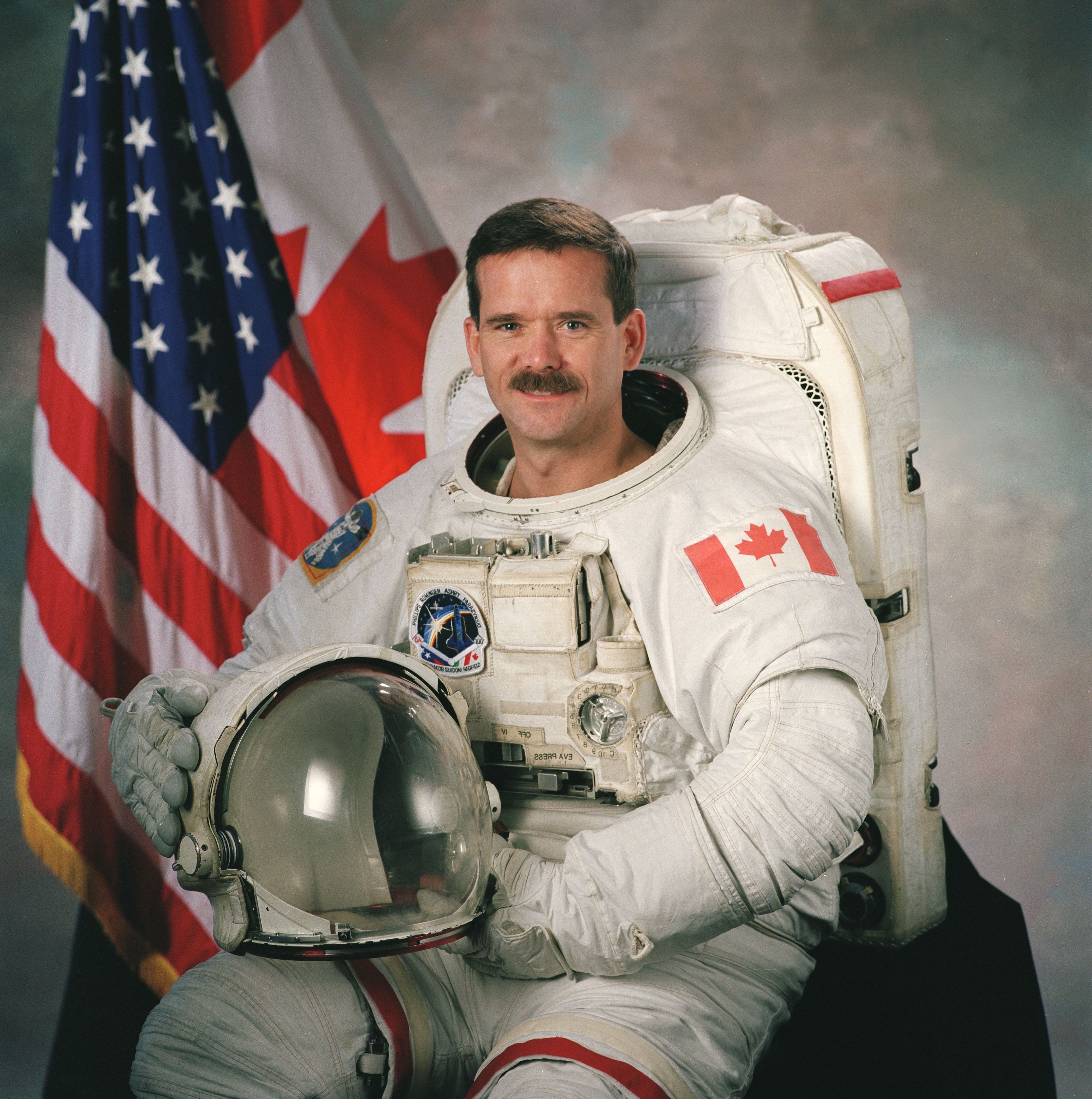 Chris Hadfield en costume de cosmonaute, son casque sur les genoux.