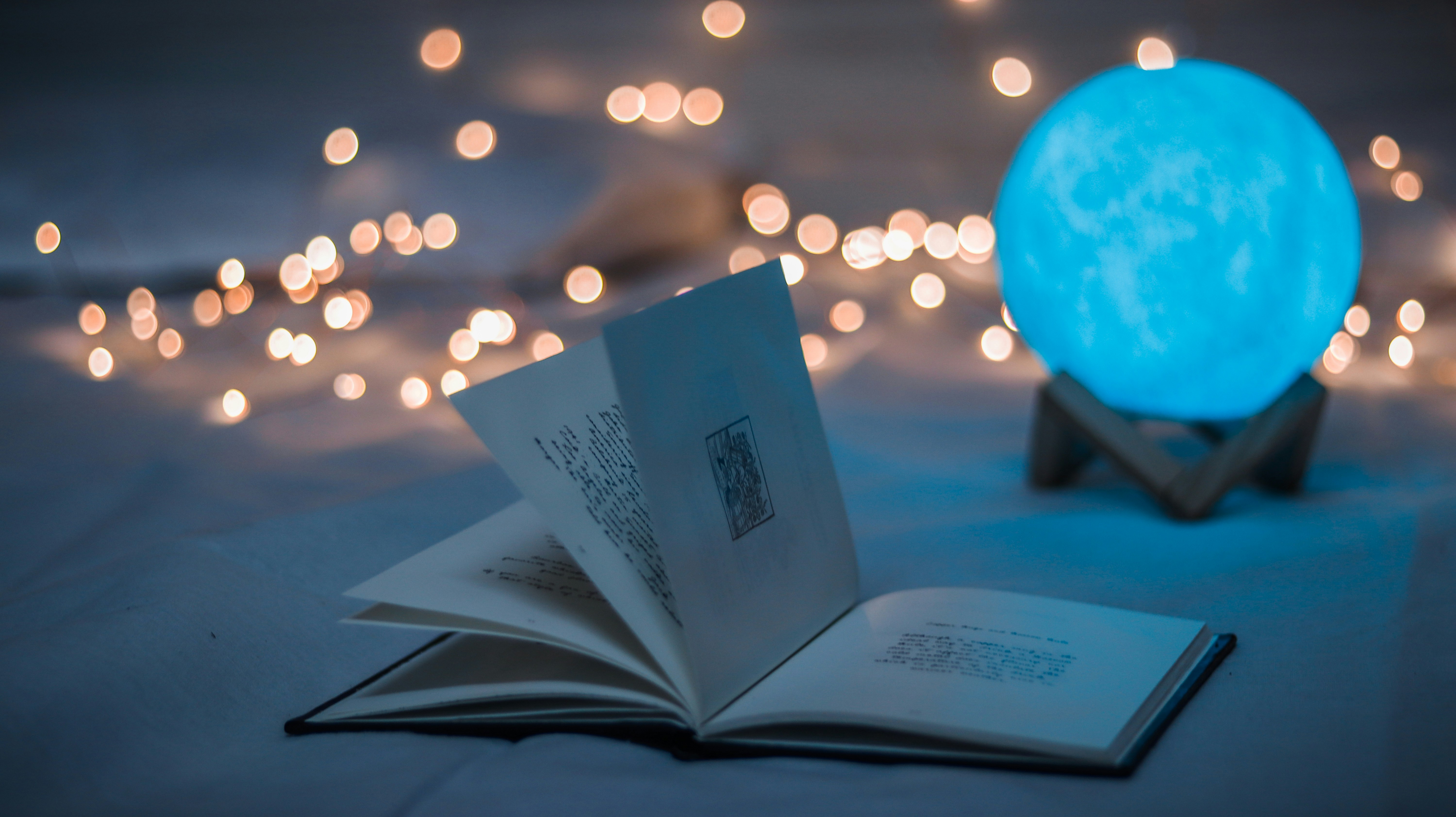 Un livre ouvert se trouve au premier plan alors qu'une boule bleue illuminée ressemblant à un globe et des guirlandes lumineuses figurent à l'arrière-plan