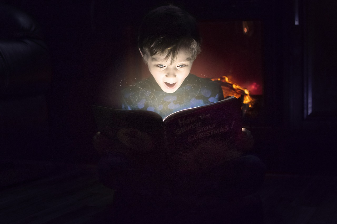 Un garçon est illuminé par le livre qu'il lit.