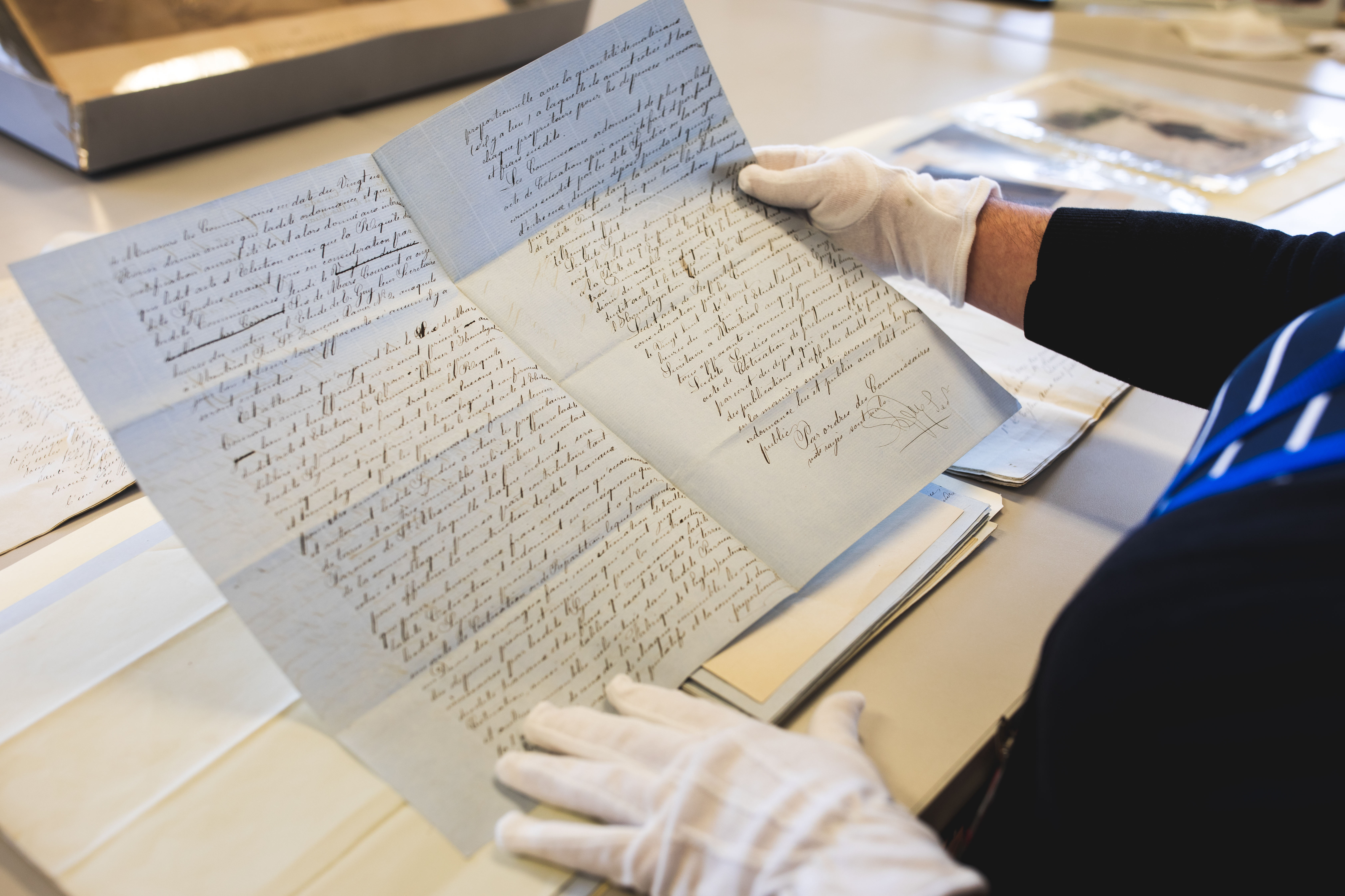 Une personne tient un document d'archives avec des gants blancs.