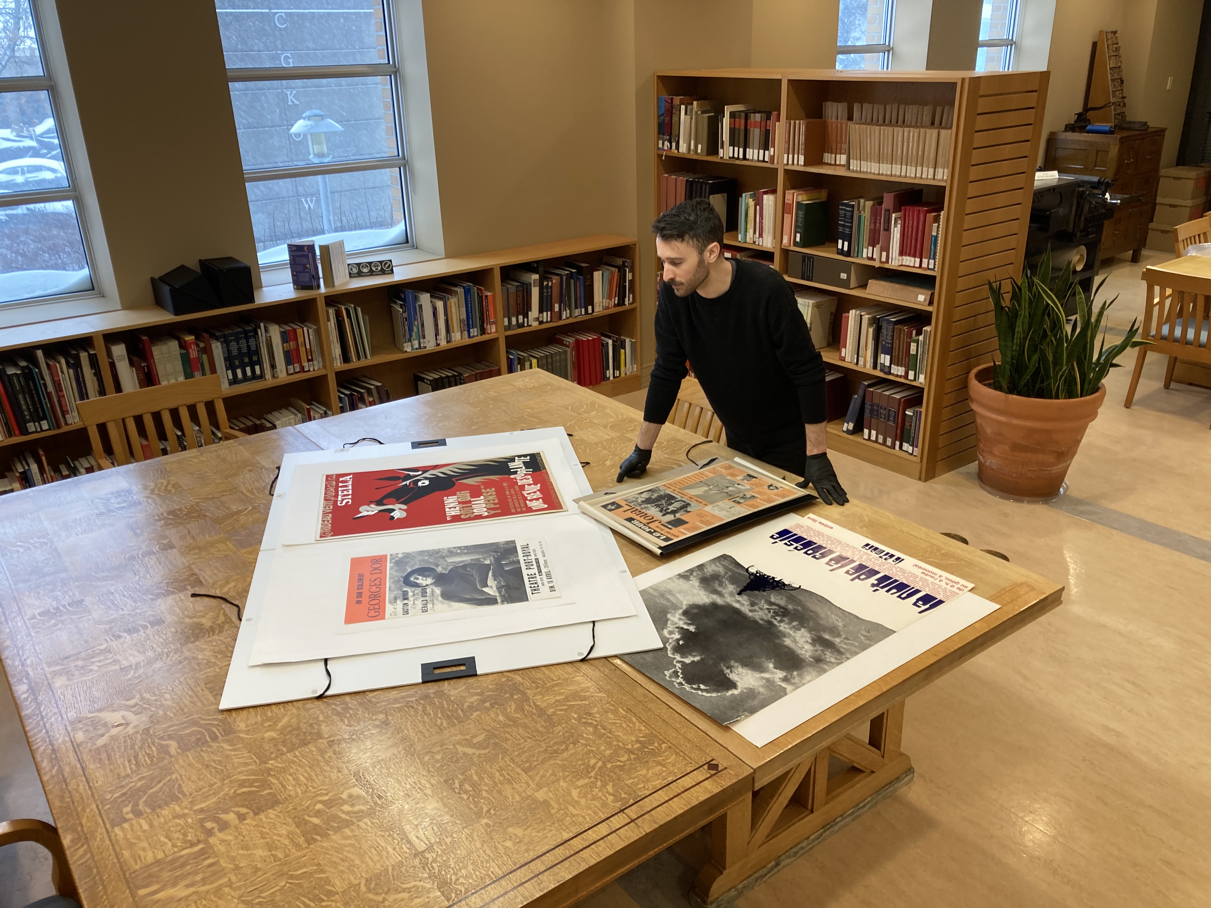 Un homme observe des affiches et des journaux sur une grande table en bois.