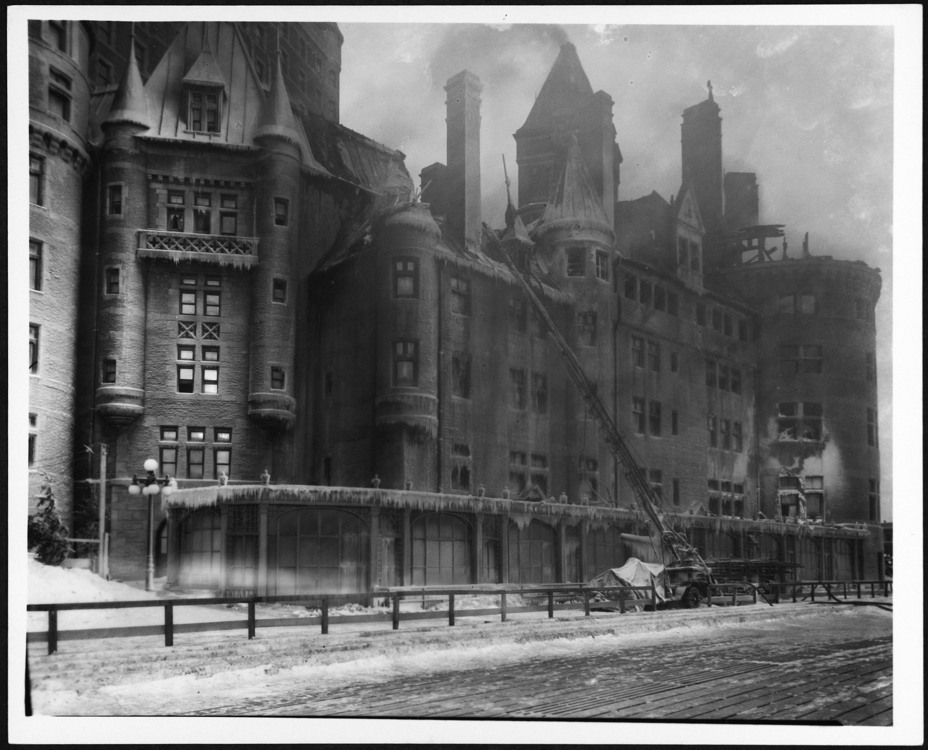 De la fumée s’échappe du Château Frontenac. Des pompiers se trouvent devant l’édifice, ainsi qu’une calèche et deux chevaux. 