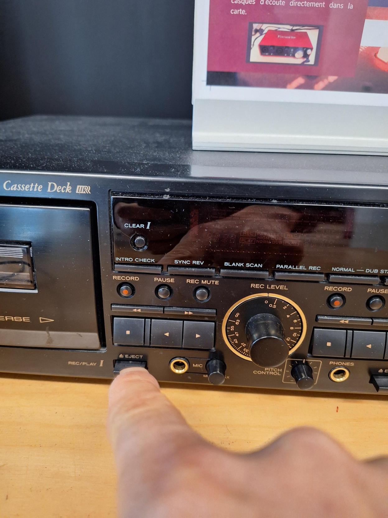 Appareil de lecture de cassette audio. Un doigt appuie sur le bouton situé juste à la droite du compartiment à cassette, en bas.