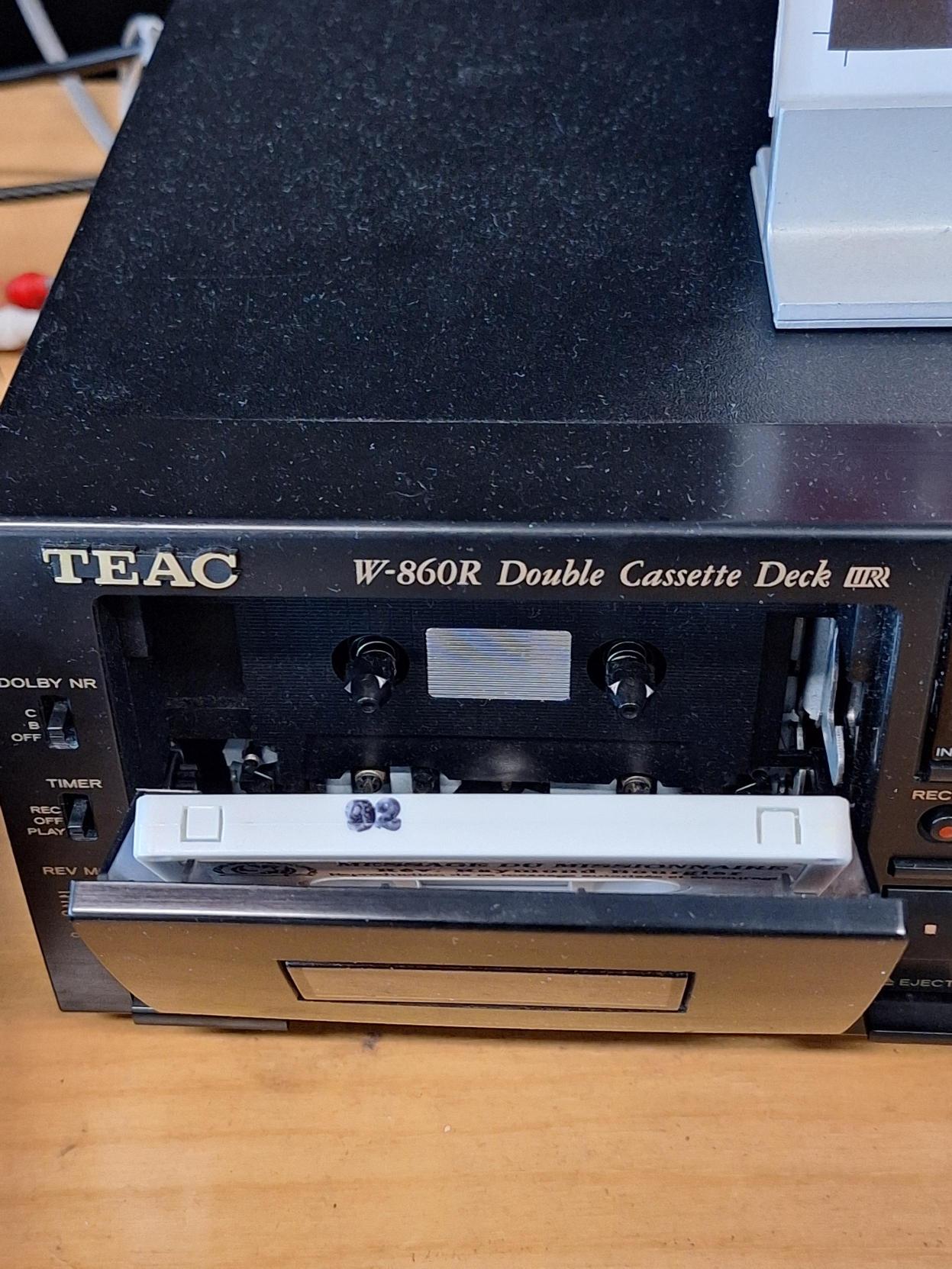 Appareil de lecture de cassette audio. Le compartiment est ouvert et on y voit une cassette, ruban vers le bas.