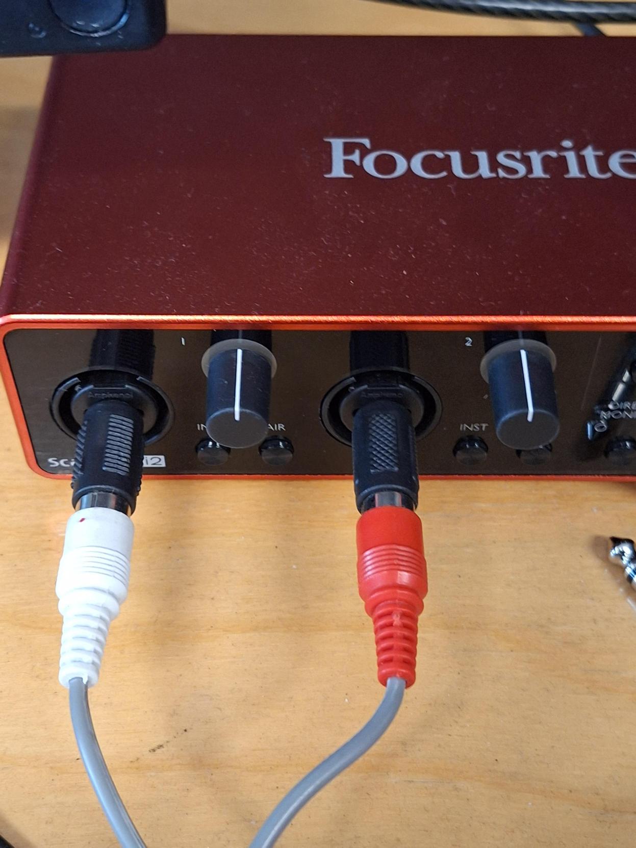 Appareil Focusrite dans lequel sont branchés deux câbles : le blanc à gauche et le rouge à droite.