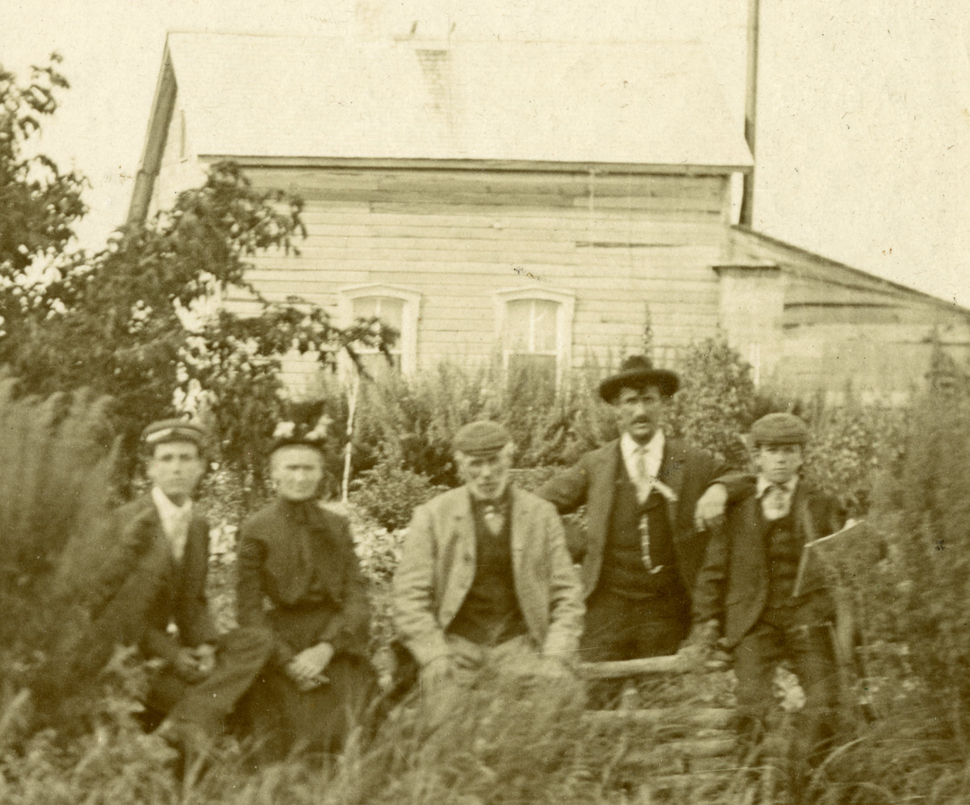 Cinq personnes assises à l’extérieur devant une maison en bois, entourées de végétation.