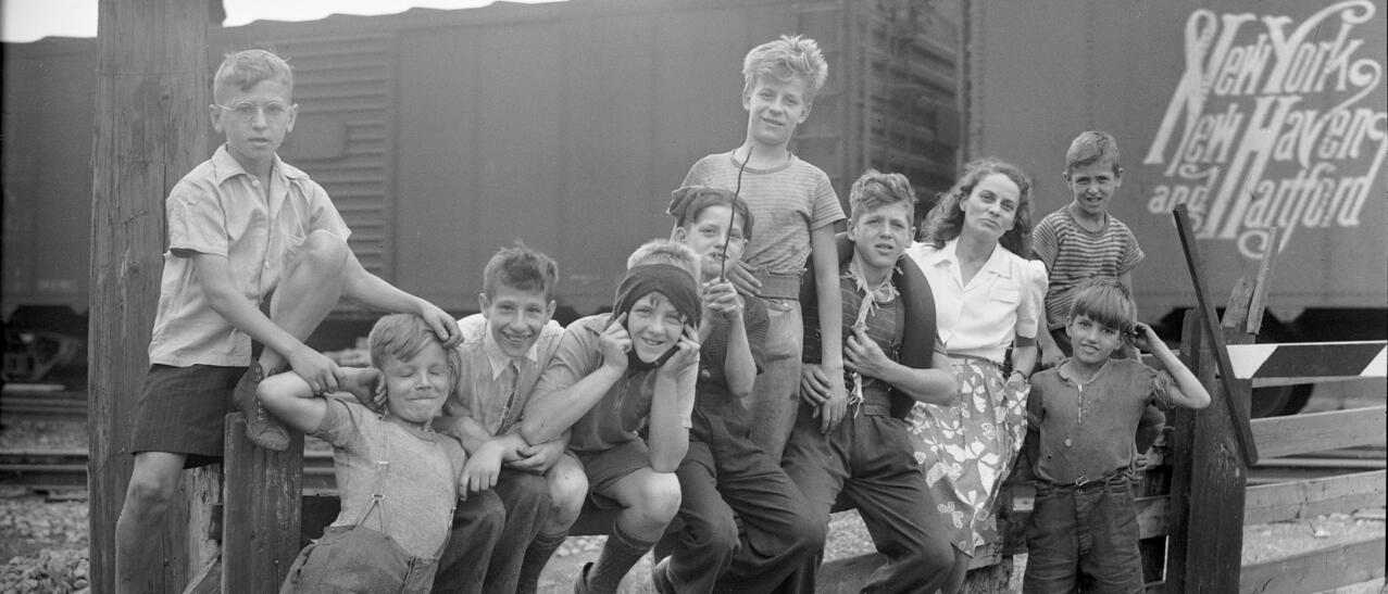 Gabrielle Roy entourée d'enfants dans le quartier Saint-Henri à Montréal. En arrière-plan des wagons de marchandise